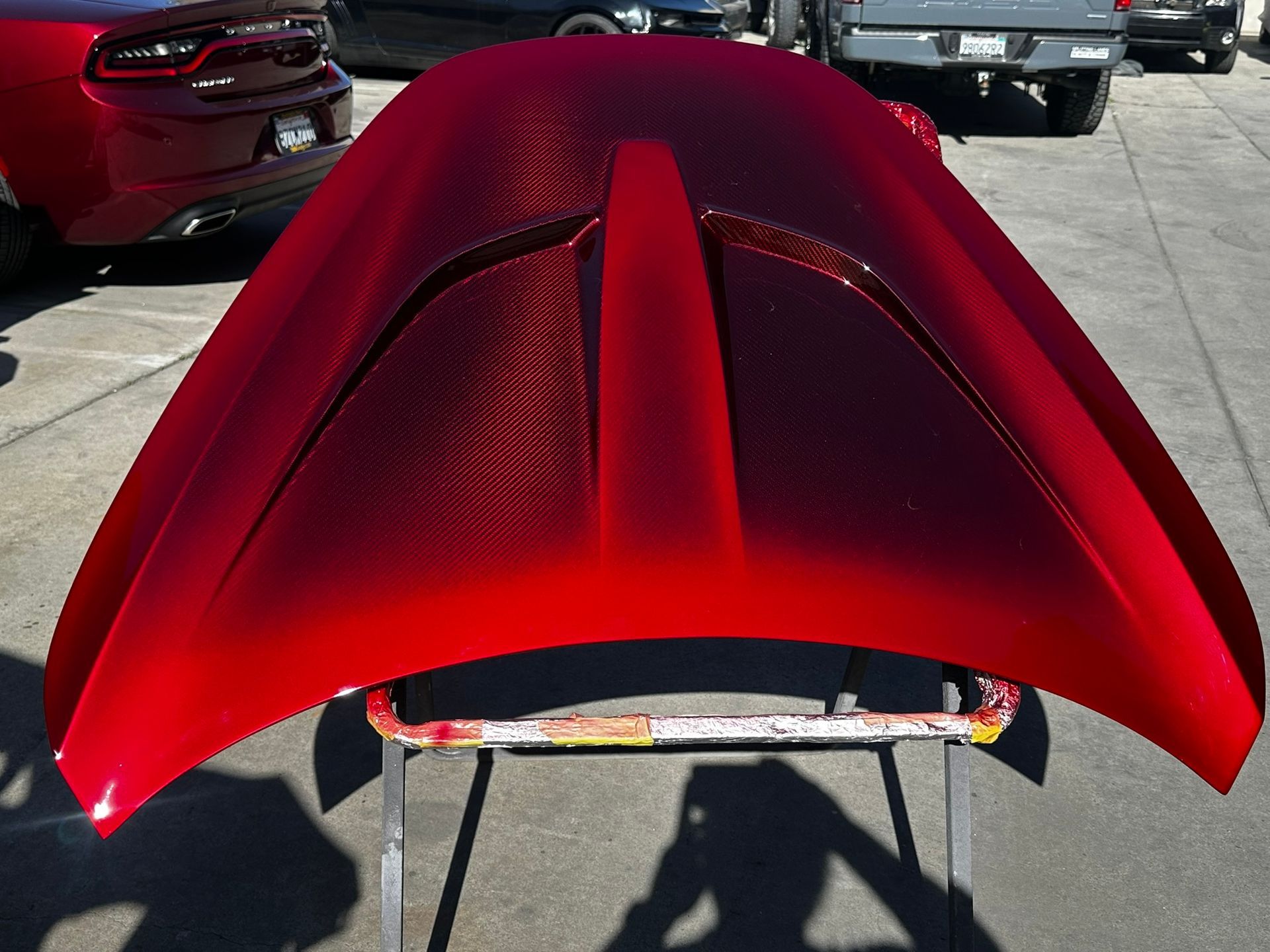 Glossy red car hood panel on pavement, viewed from above in a parking lot
