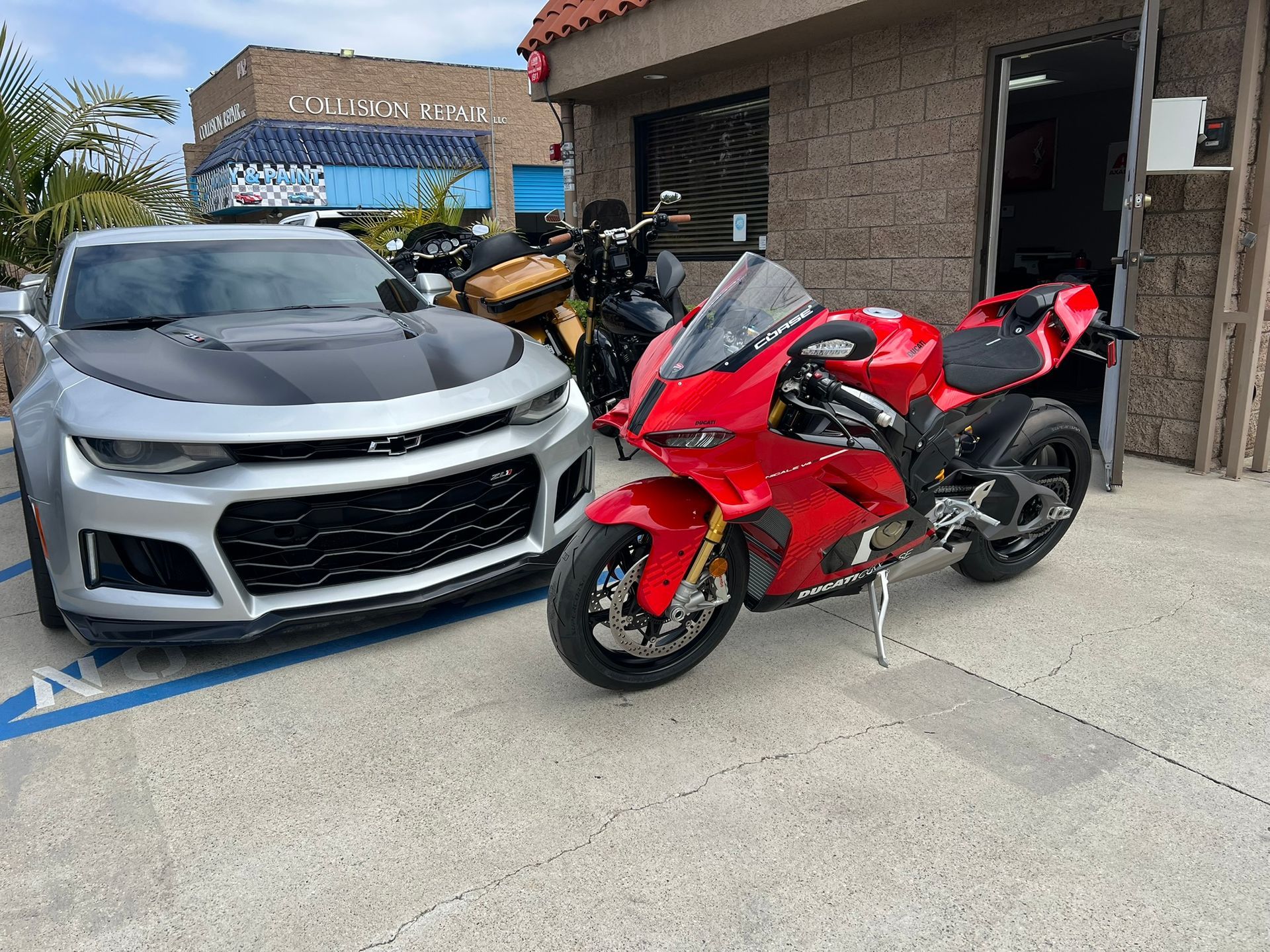 Red sport motorcycle parked beside a silver sports car in a driveway next to a brick house