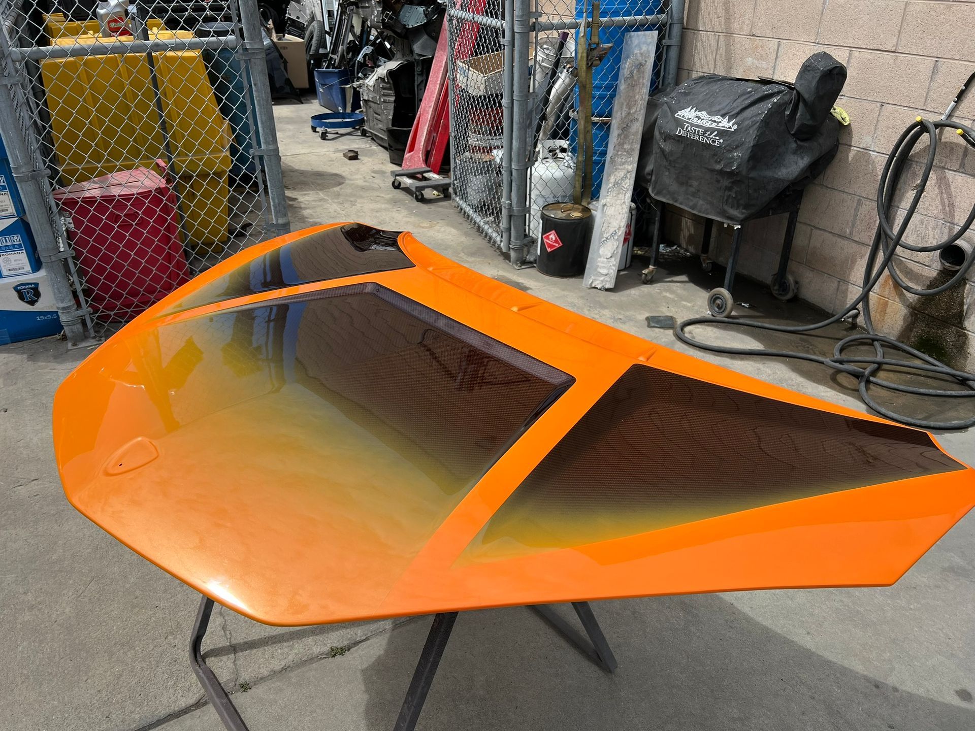 Orange streamlined car body shell in a workshop, with a dark tinted windshield and black stand.