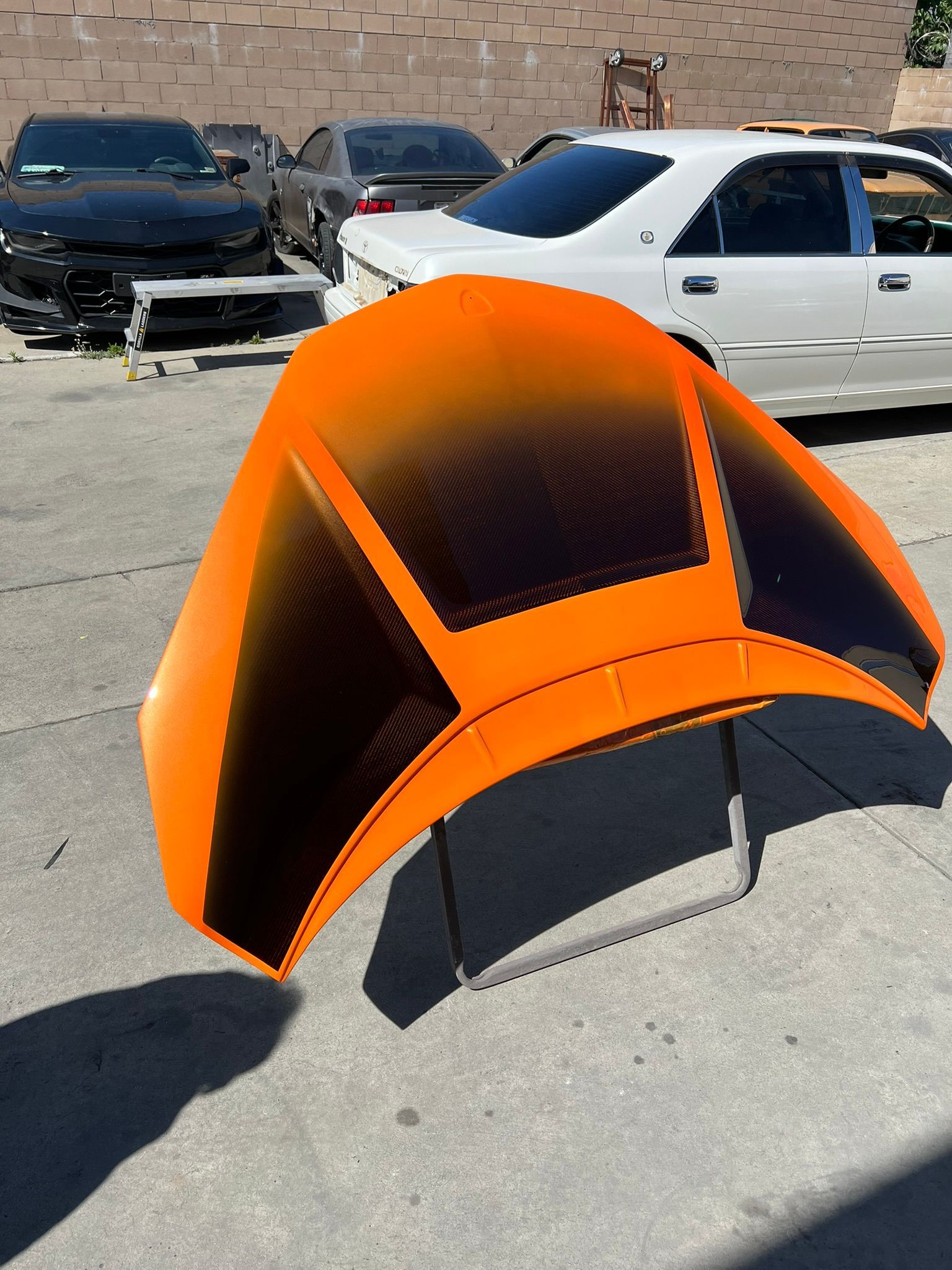 Orange-and-black tent-like car sunshade on a sunlit parking lot, with parked cars and a brick wall behind it