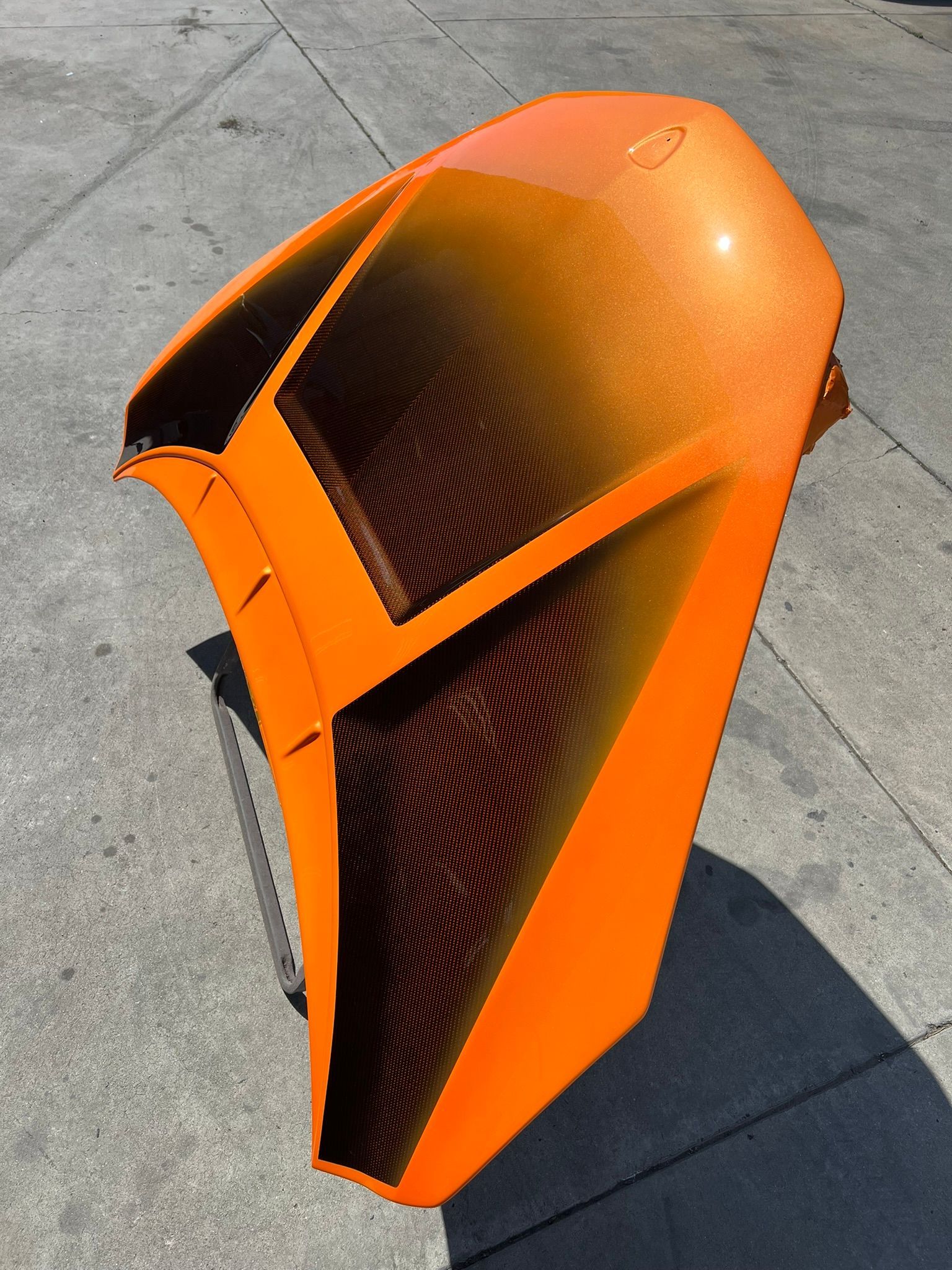 Orange carbon-fiber car body shell on pavement, shown from above.
