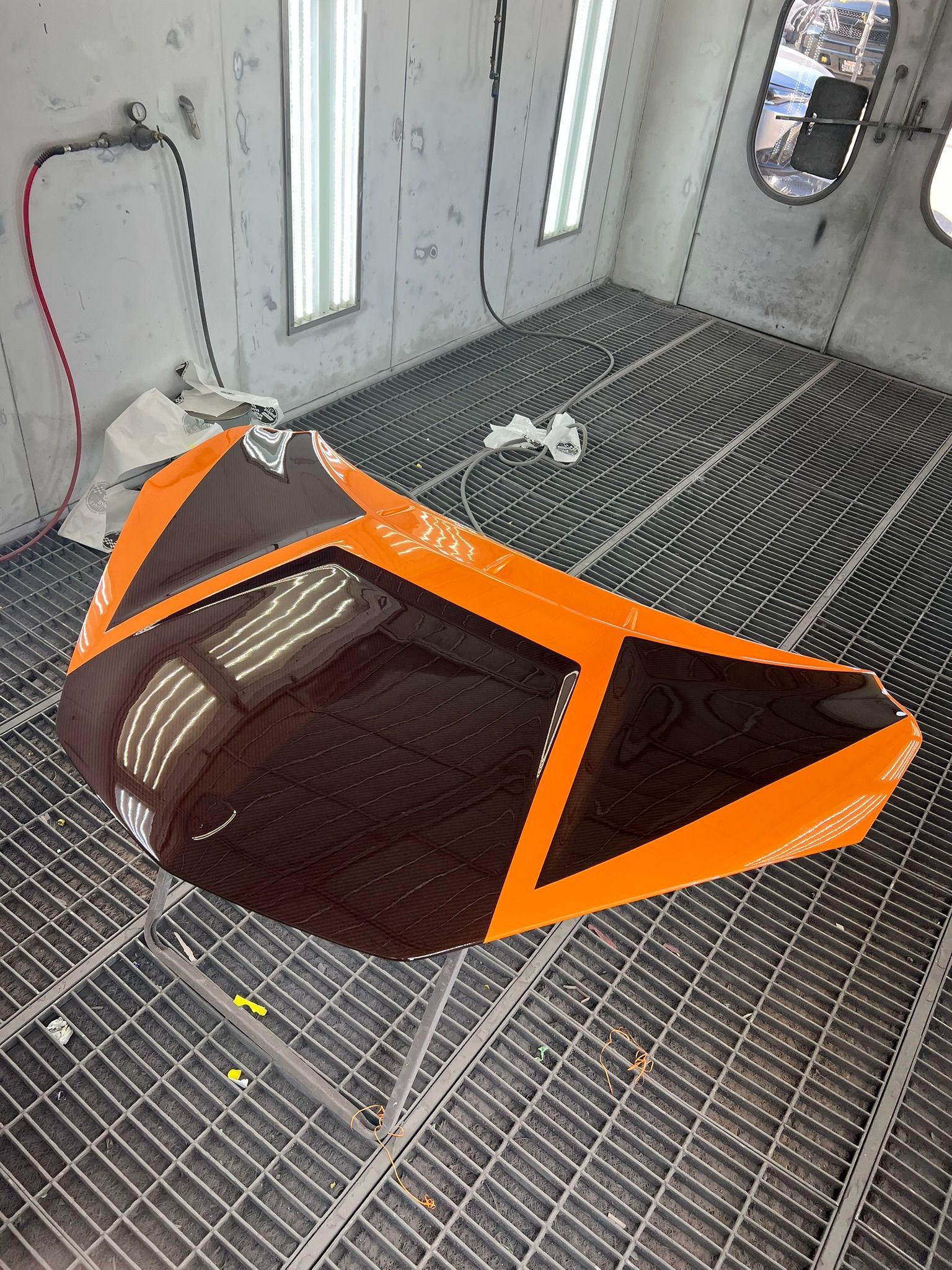 Orange-and-black automotive body panel lying on a metal grate in a spray booth