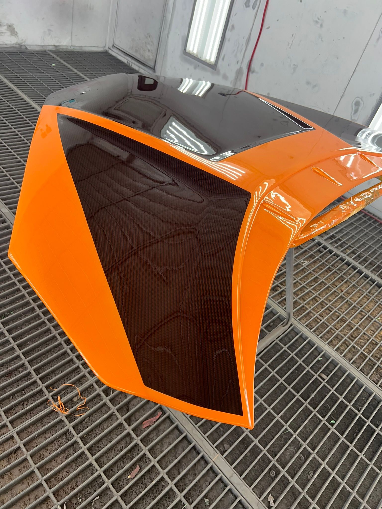 Orange and black sports car hood and front fender in a spray booth