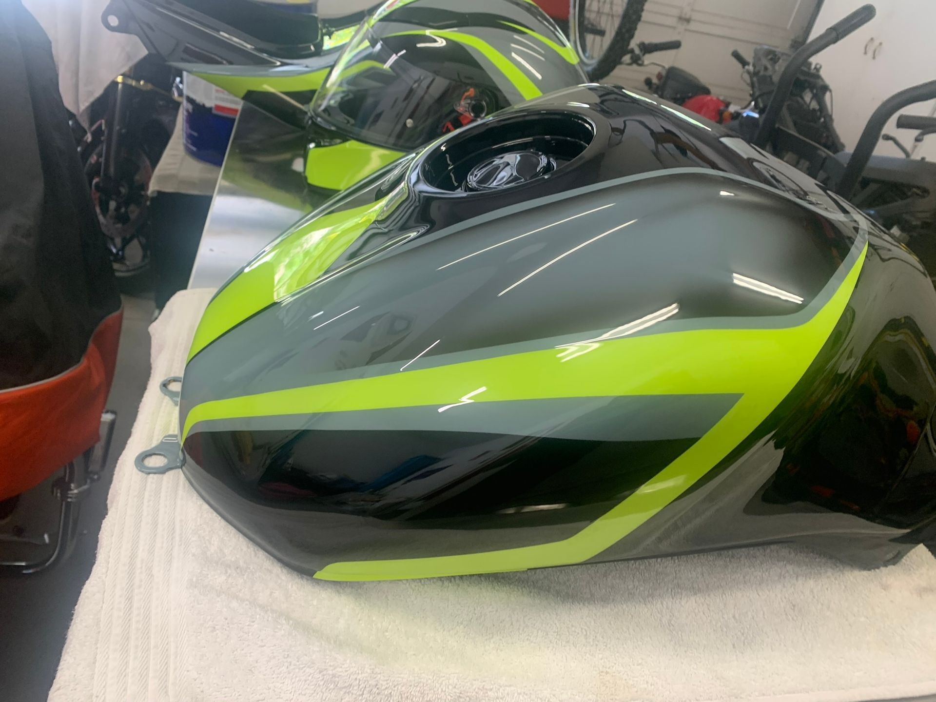 Gray and neon green motorcycle fuel tank on a workbench in a garage