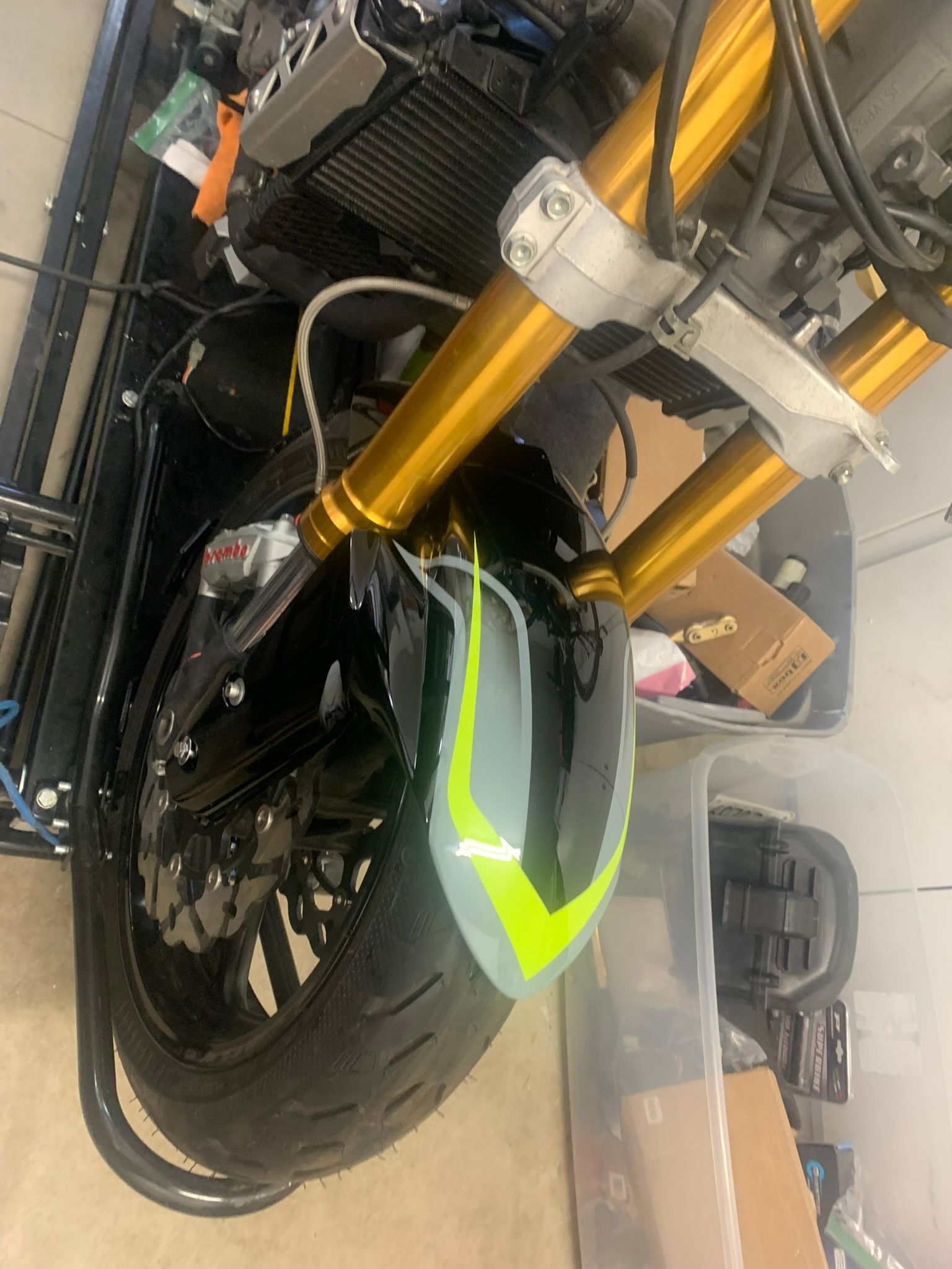 Close-up of a black motorcycle front wheel with gold forks and a neon green accent in a garage.