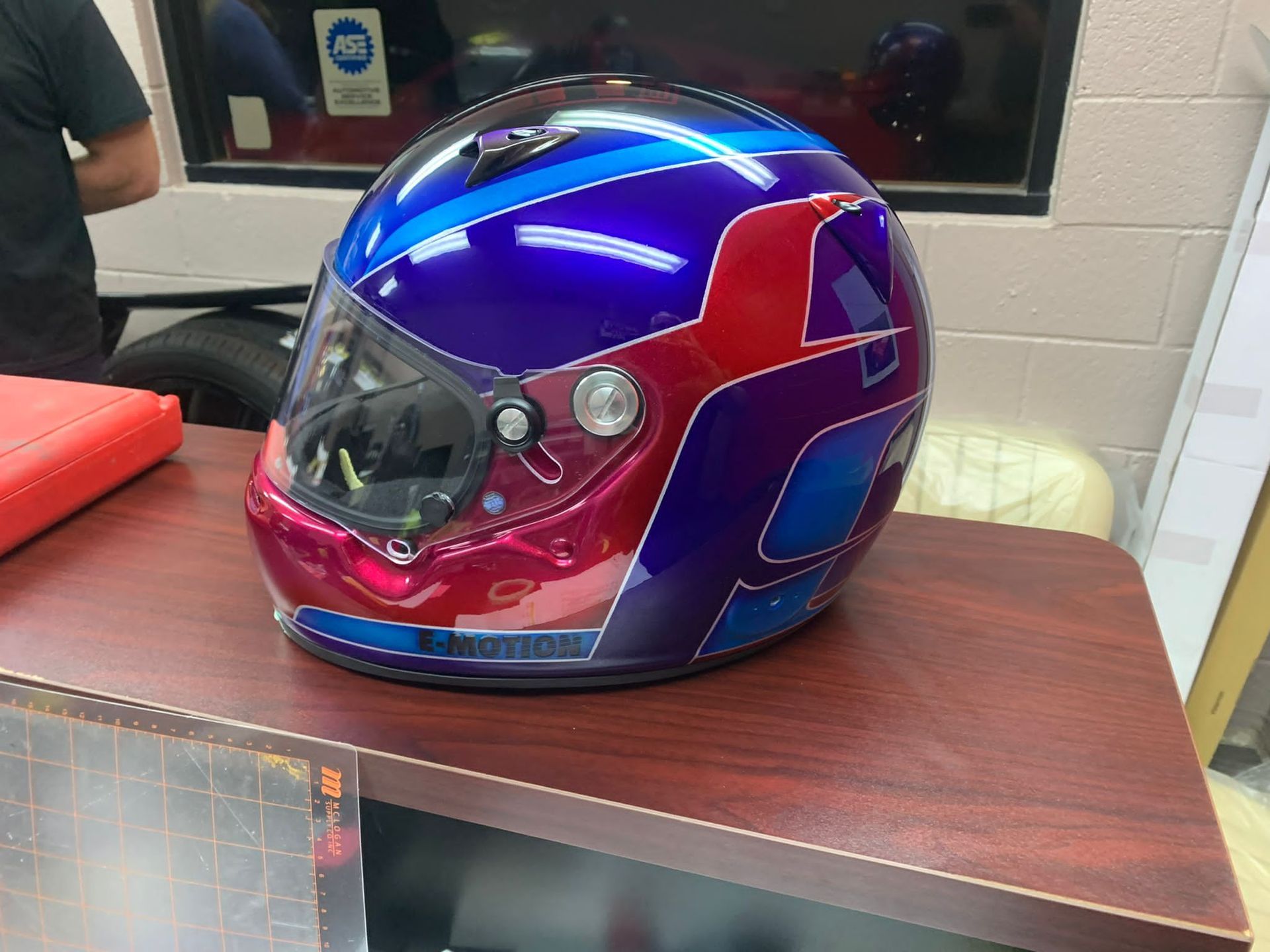 Blue and pink full-face motorcycle helmet on a wooden desk in a classroom-like setting