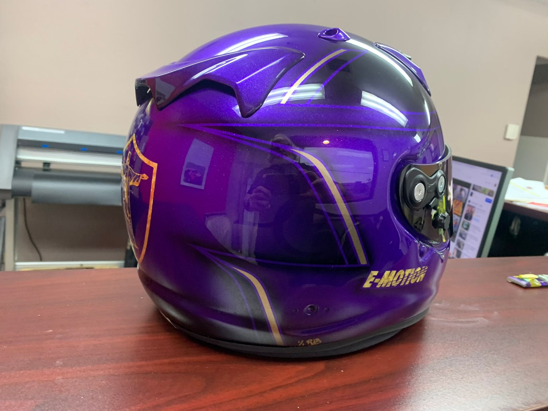 Purple motorcycle helmet on a wooden desk, with a glossy finish and a gold logo.