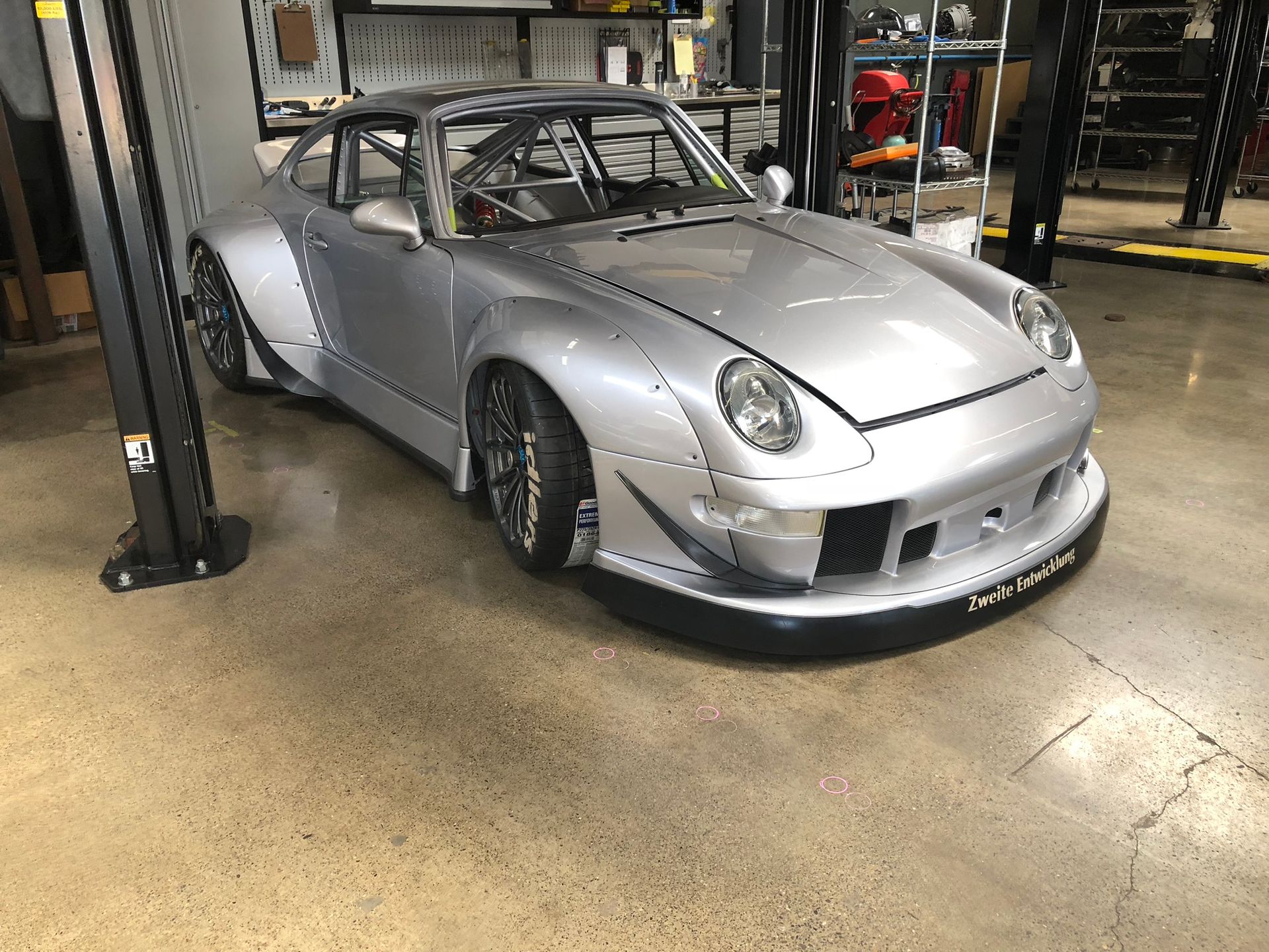 Silver sports car in a garage, viewed from the front-left with a low stance and wide body kit