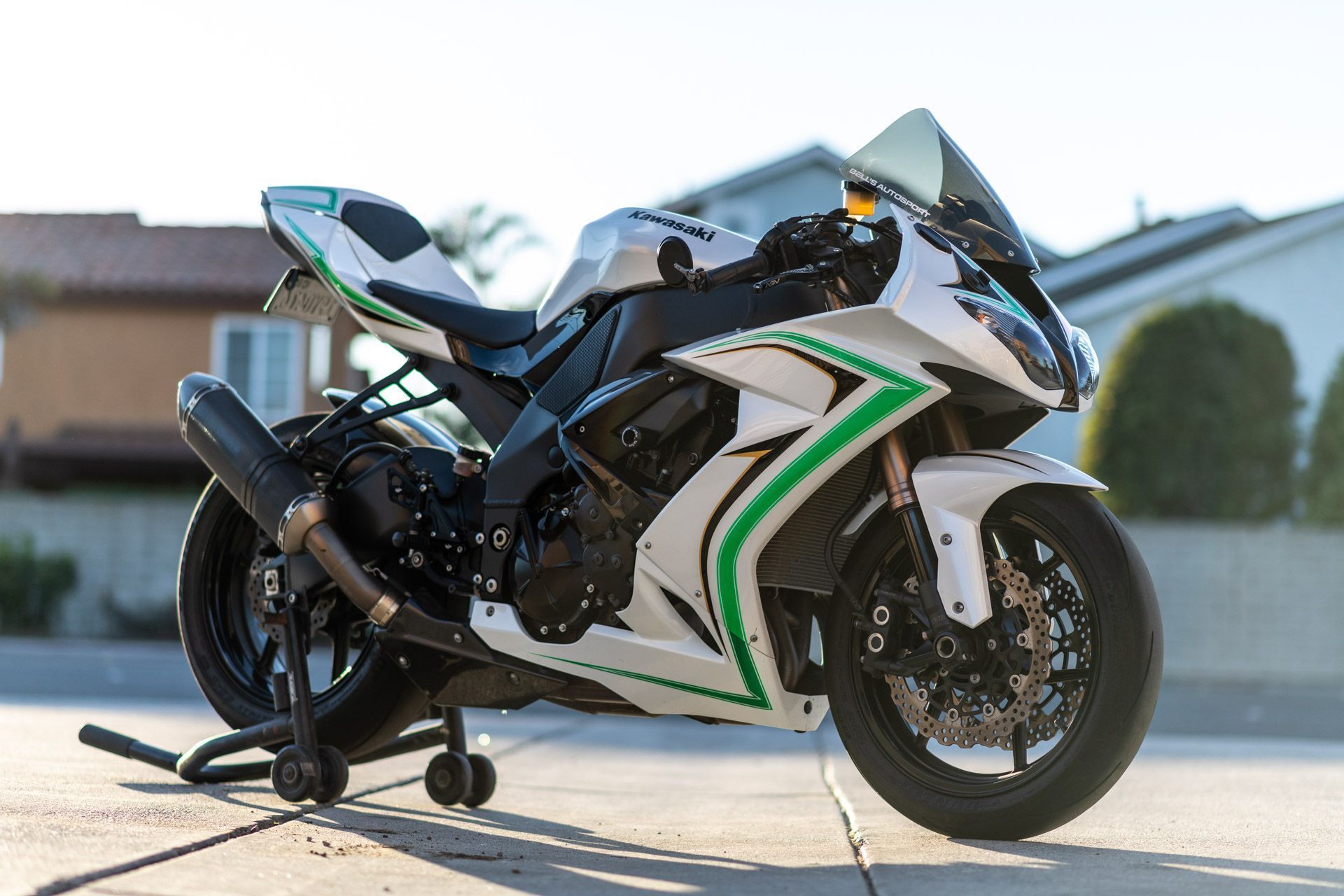 White and green sport motorcycle parked on a driveway in front of a suburban house