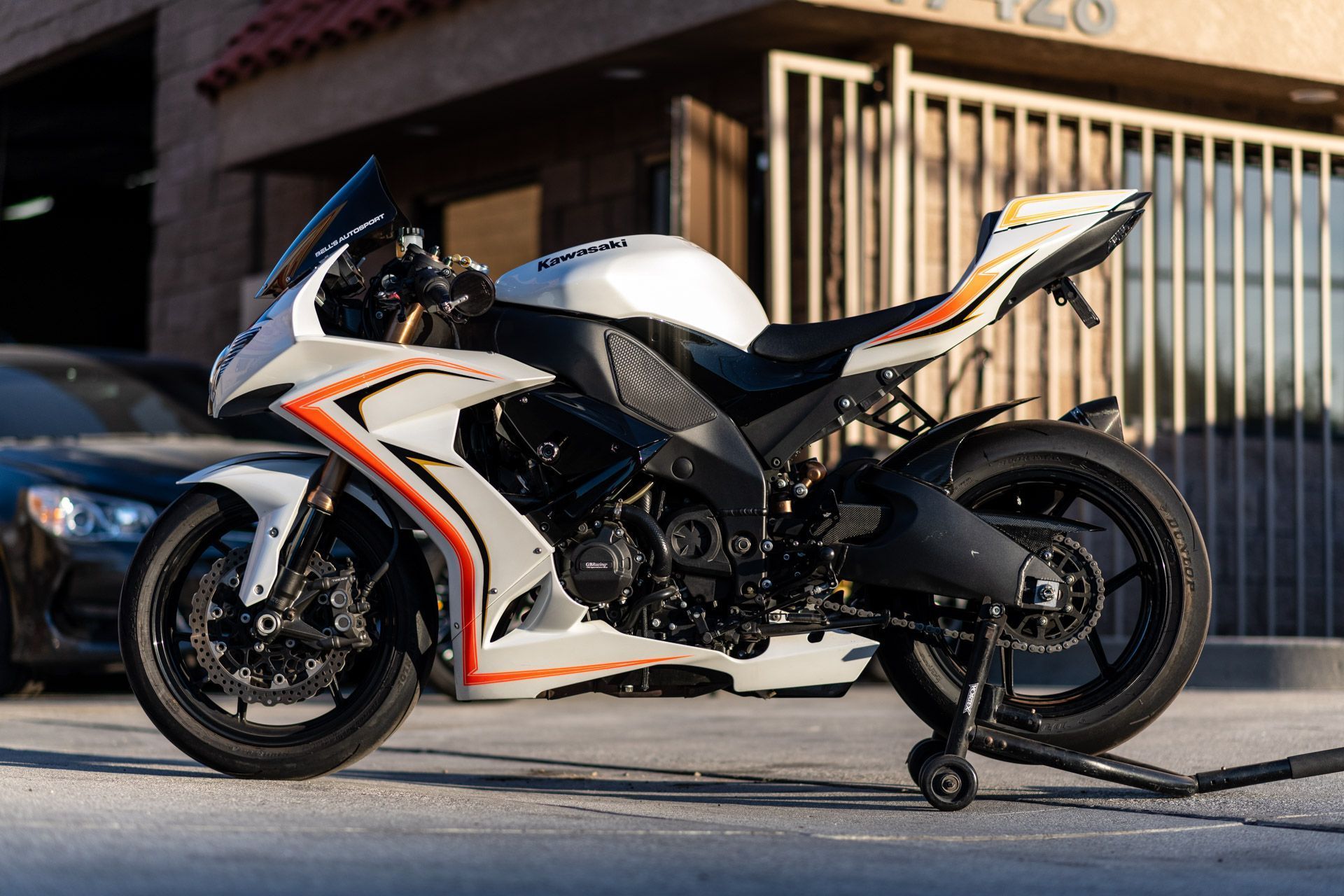 White, black, and orange sport motorcycle parked on a street in front of a building and metal gate