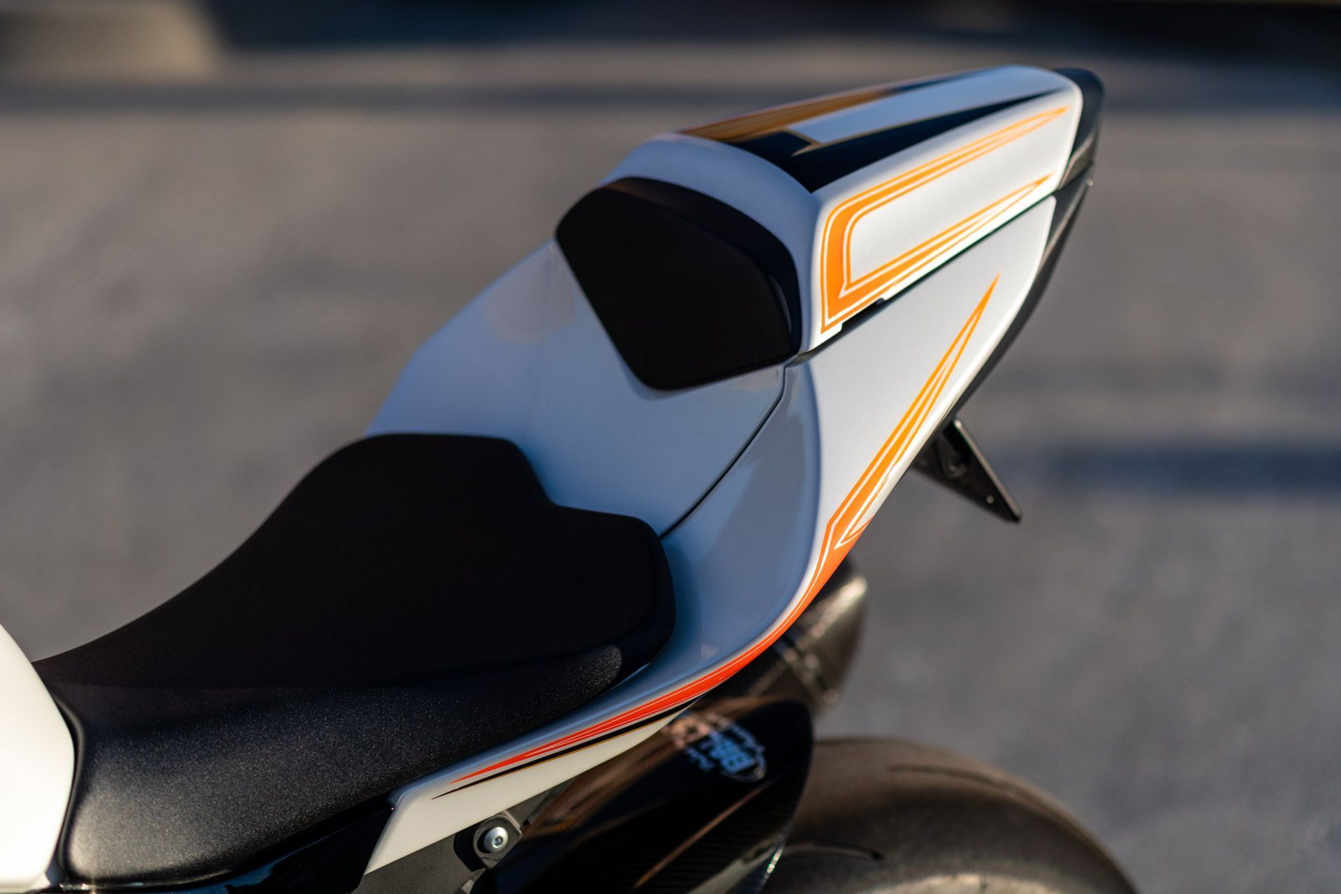 Close-up of a white and black motorcycle seat and rear fairing with orange accents