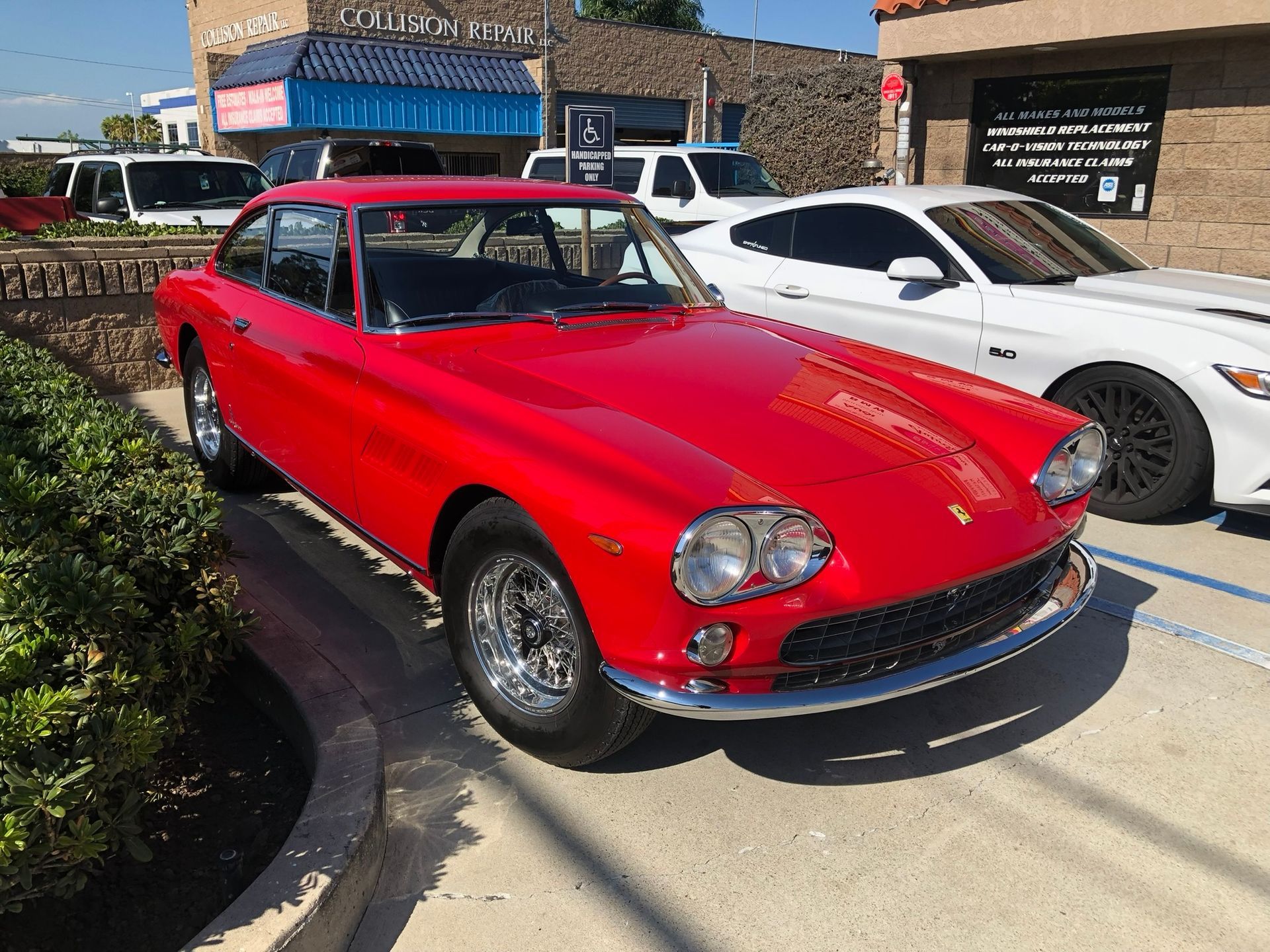 Red classic coupe parked outdoors beside a white sports car on a sunny street