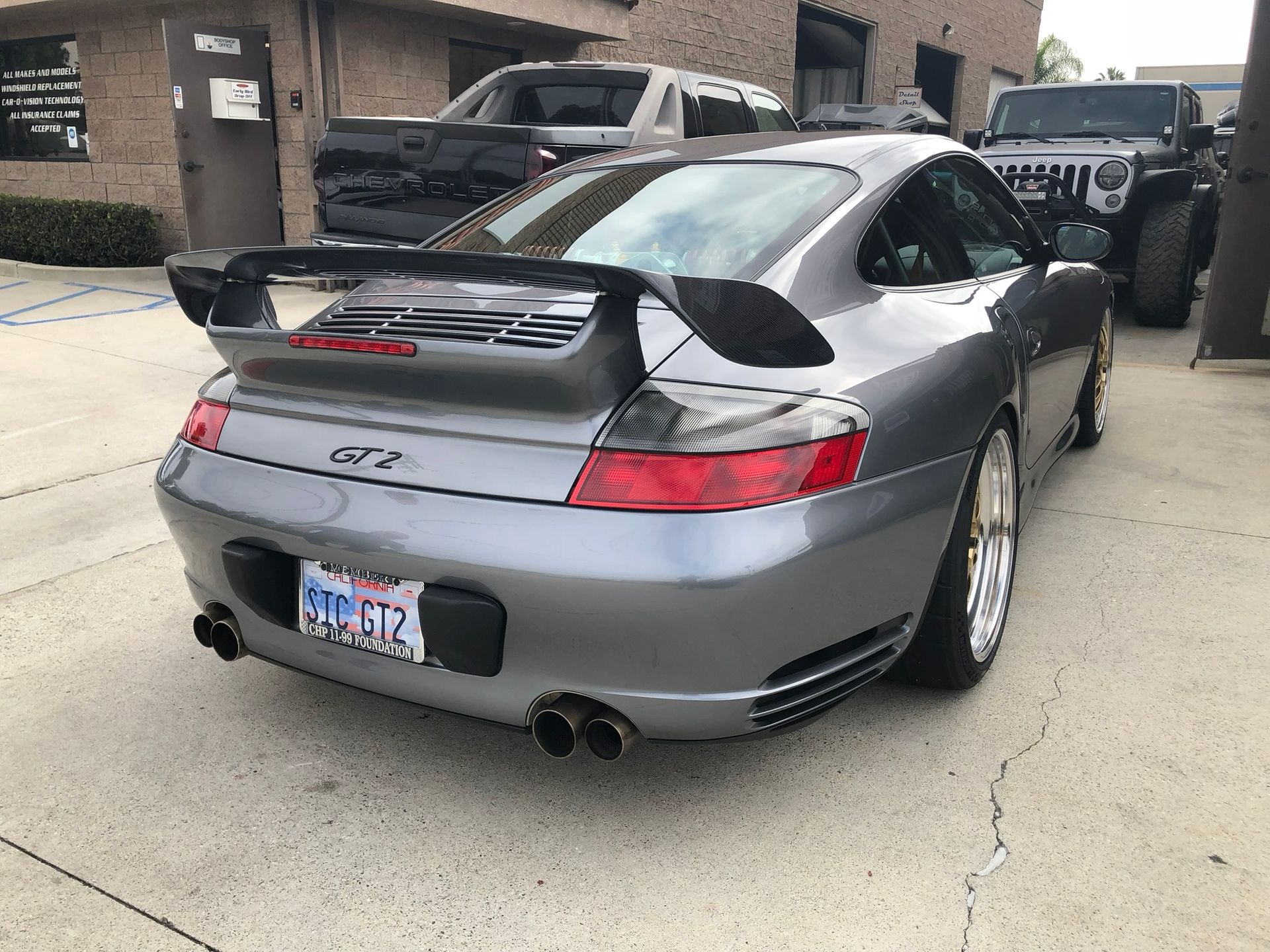 Silver Porsche GT3 parked on a driveway, rear view with large spoiler and dual exhausts