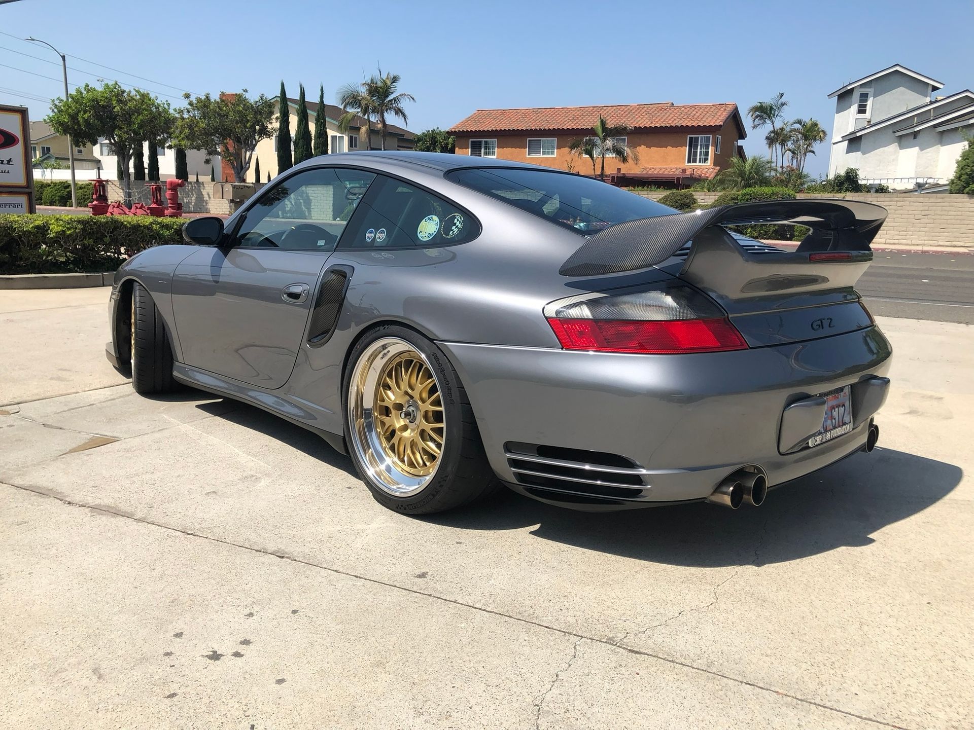 Gray sports car with gold wheels parked outdoors, rear three-quarter view.