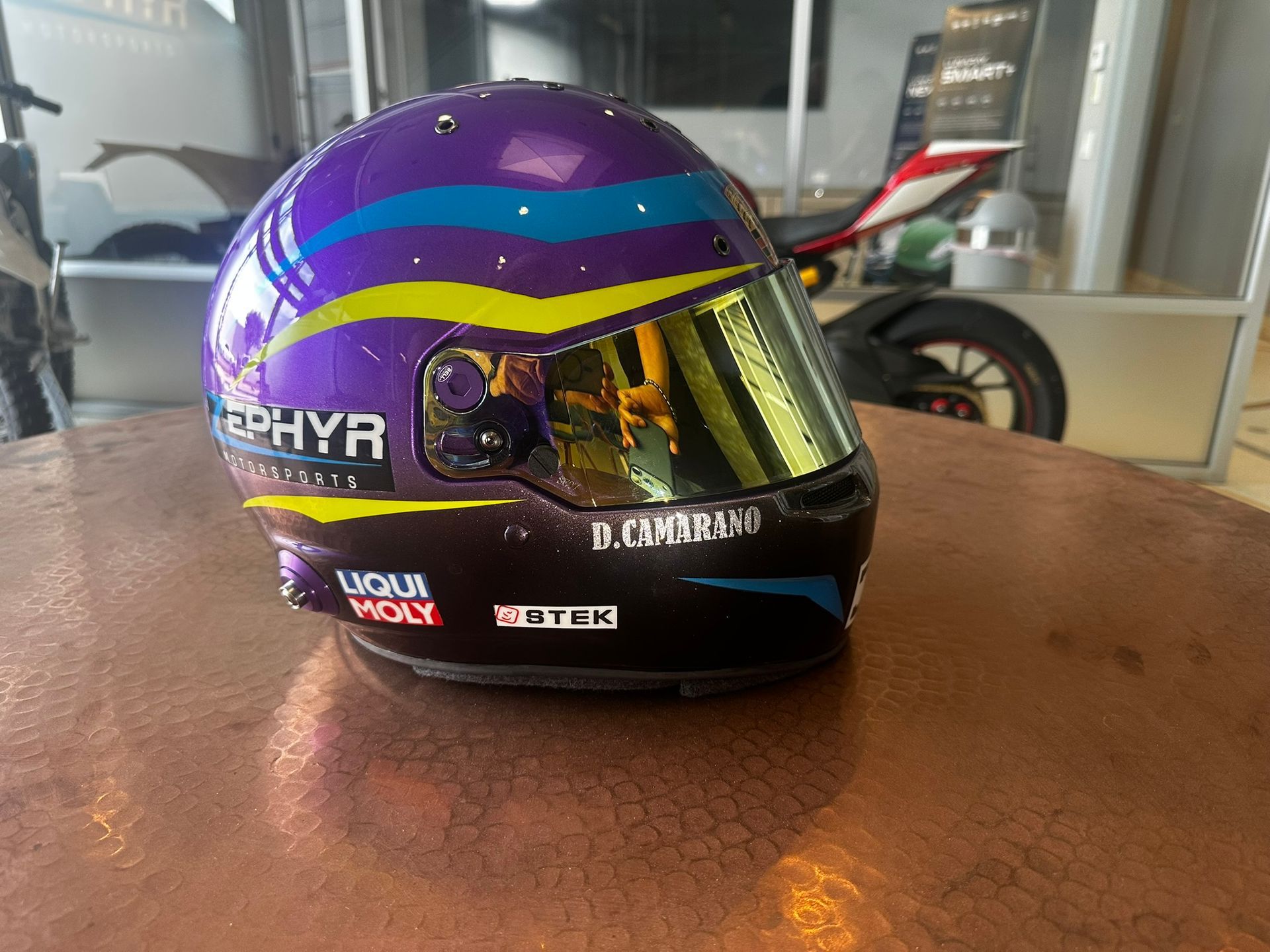 Purple-and-cyan motorcycle helmet with a gold visor on a table indoors