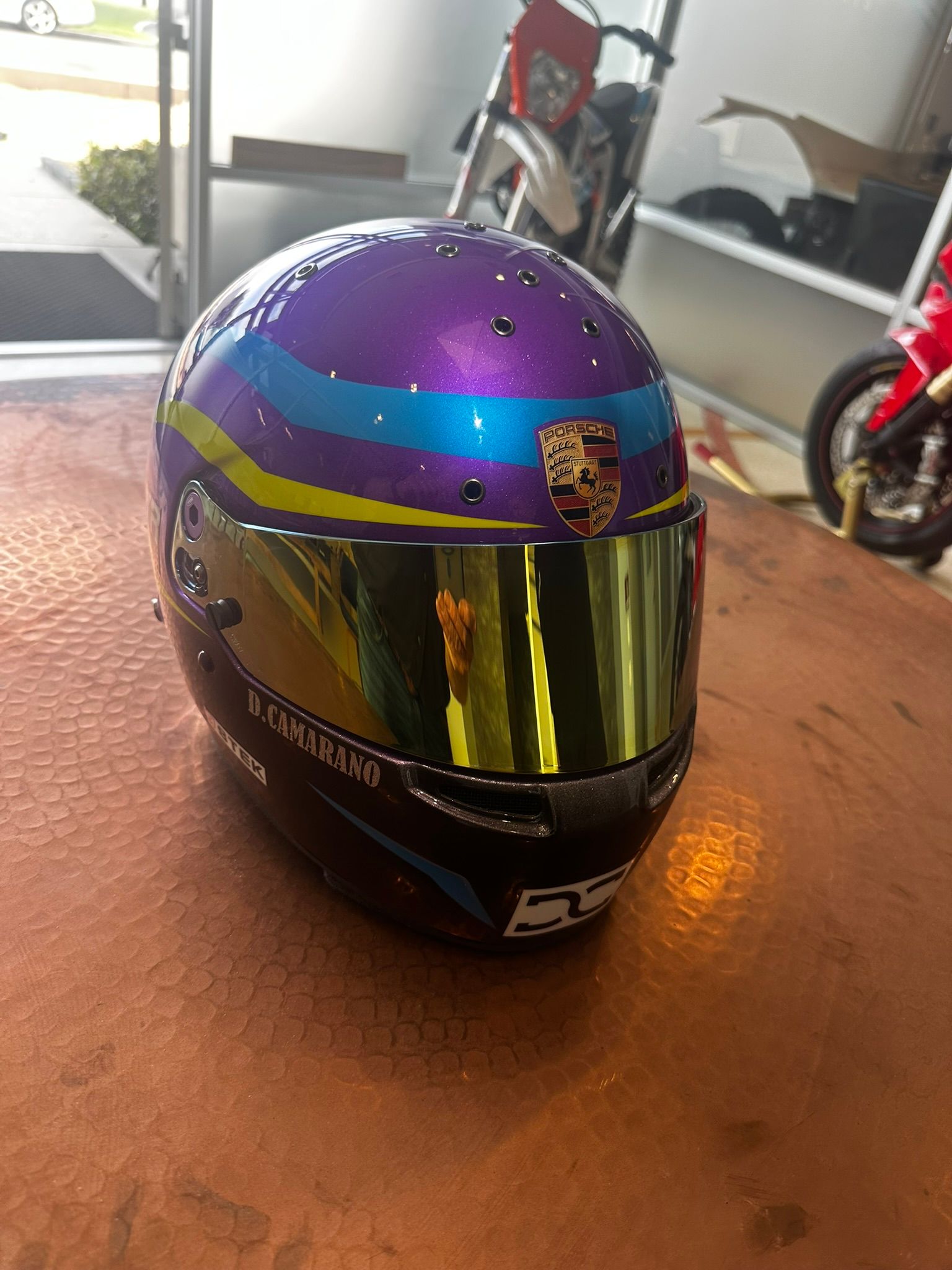 Purple motorcycle helmet with gold visor and colorful stripe sitting on a wooden table
