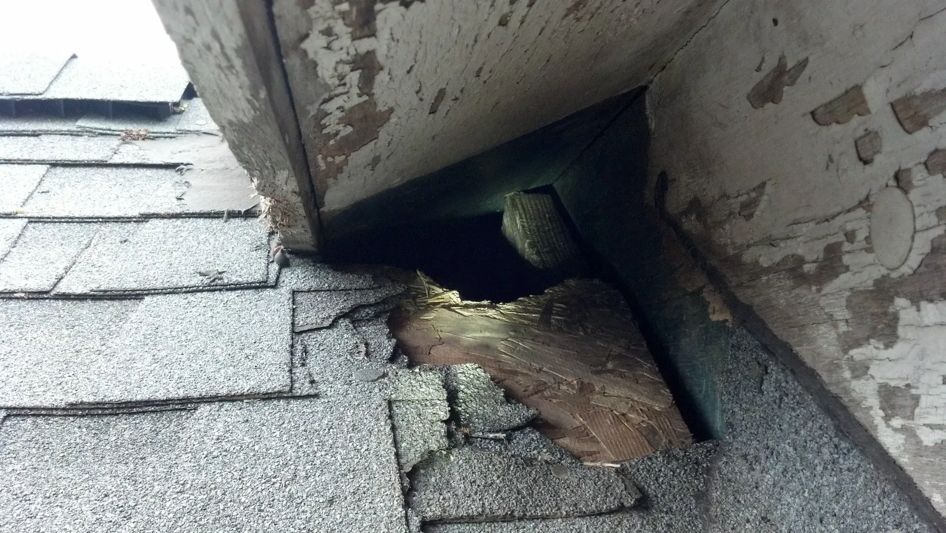 Damaged roof section with hole, revealing dark interior. Wood rot, peeling paint.