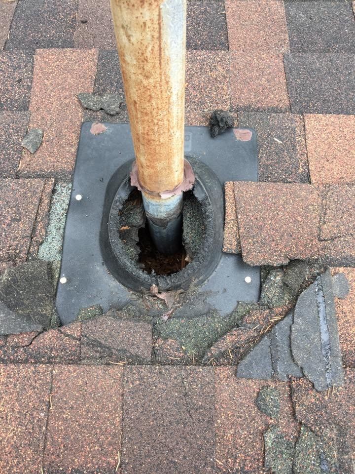 Roof damage around a rusty pipe. Shingles are broken and missing.