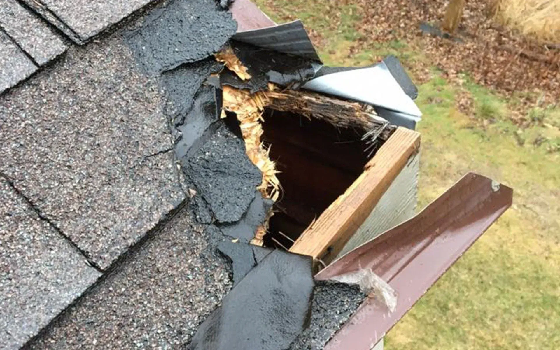 Damaged roof corner with missing shingles and exposed wood, brown gutter.