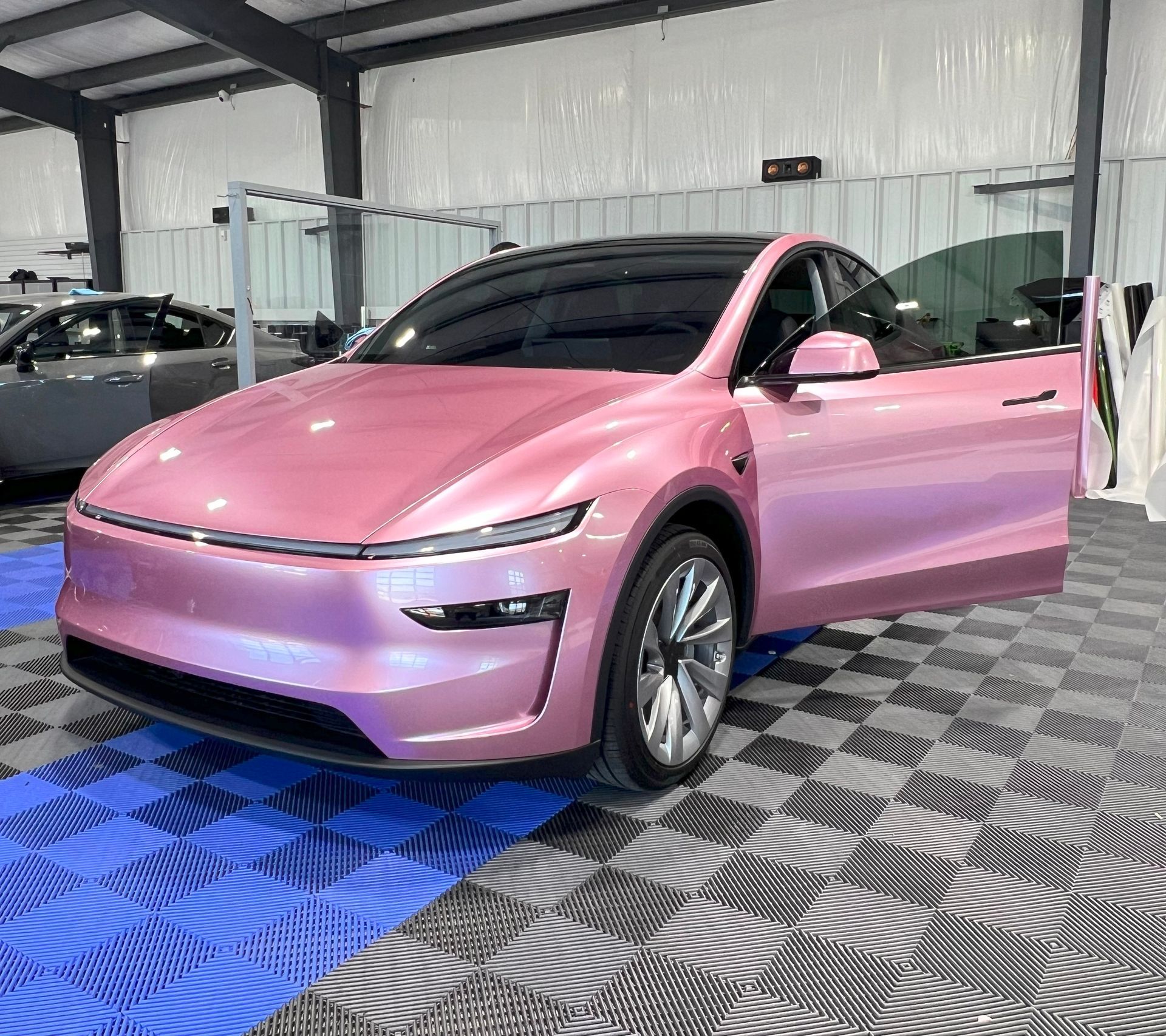Pink Tesla car with open door in a shop with checkered floor.