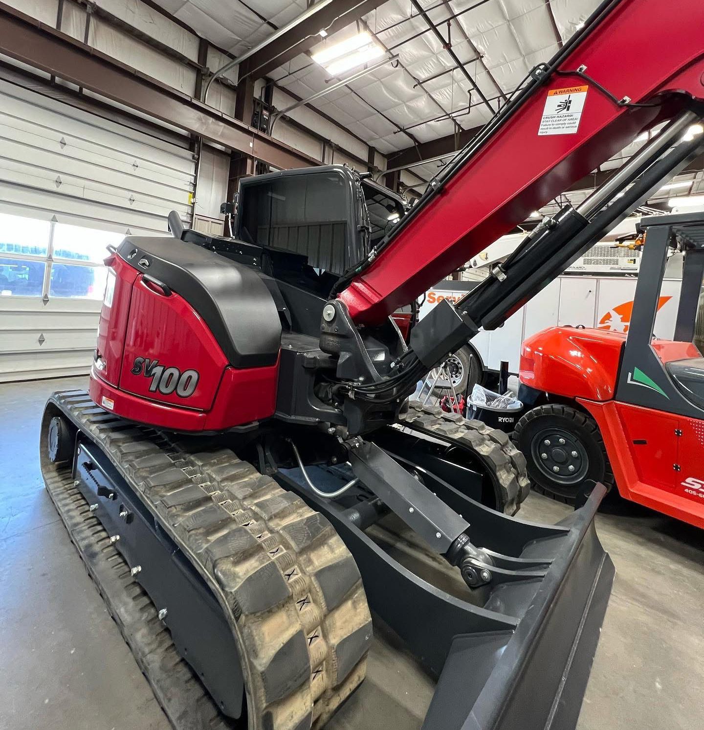 Red and black excavator with tracks inside a shop.