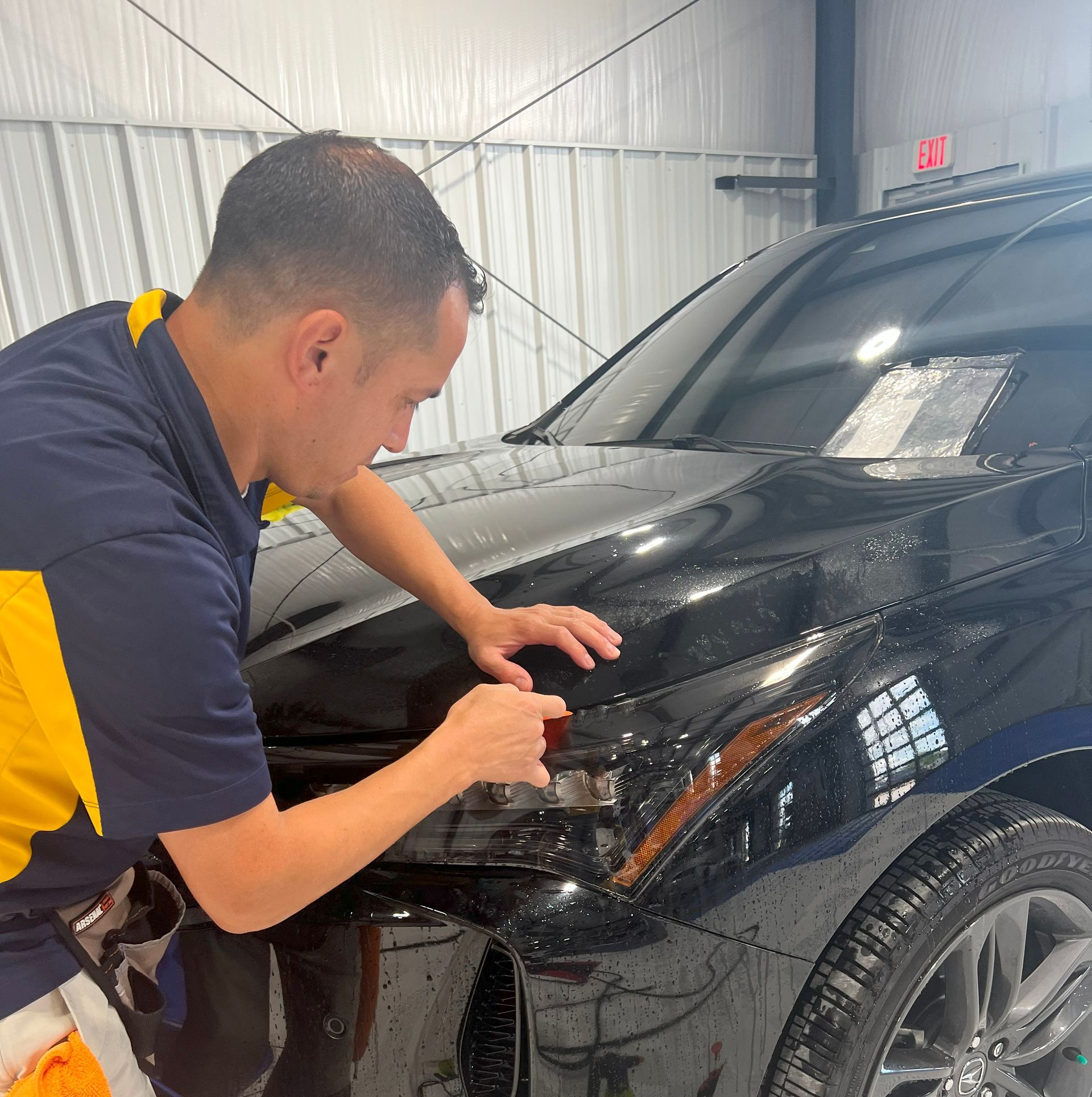 Man applying tint to a black car headlight in a garage.