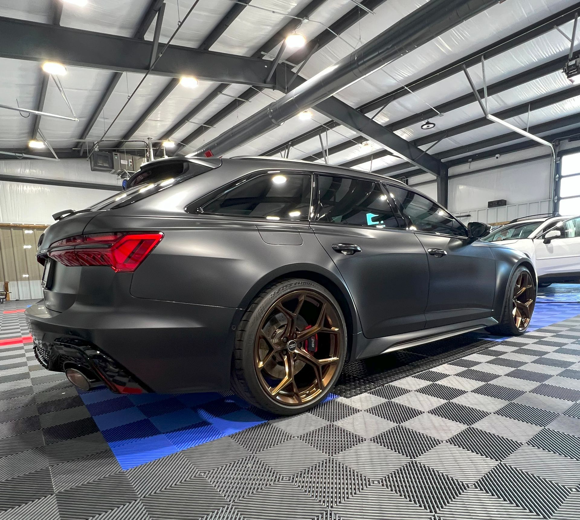 Matte black Audi RS6 Avant wagon with bronze wheels in a garage with tiled floor.