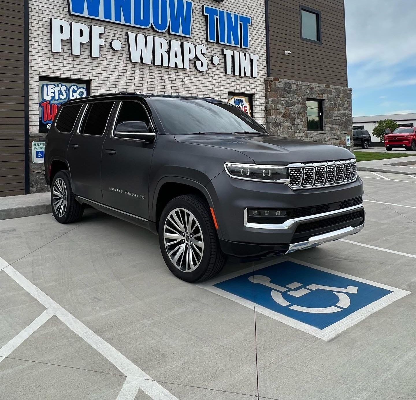 Dark gray SUV parked in a handicap spot in front of a window tinting business.