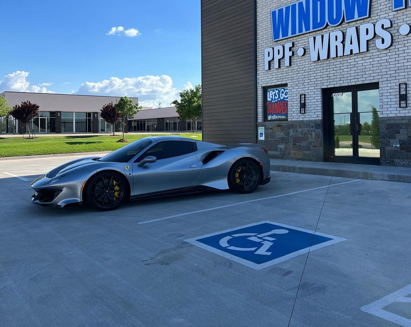 Silver Ferrari parked in a handicapped parking spot in front of a window tinting business.