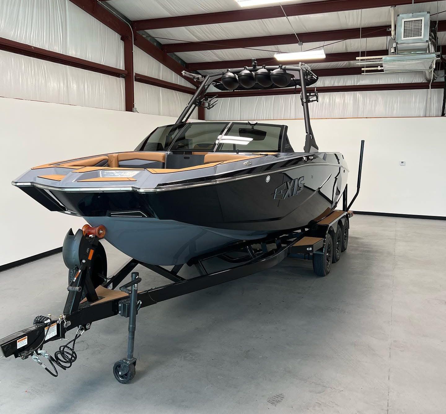 Black and gray wakeboard boat on a trailer inside a metal building.