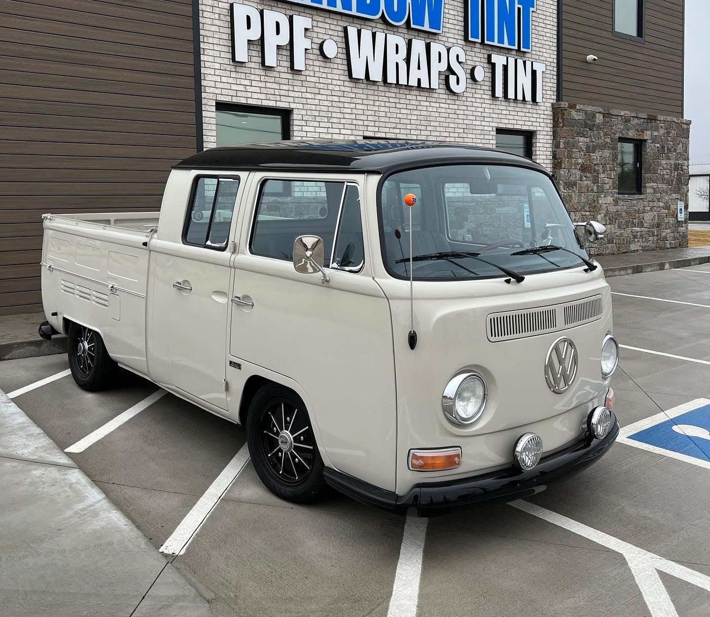 Beige Volkswagen Type 2 pickup truck with black roof parked in front of a building with signage.