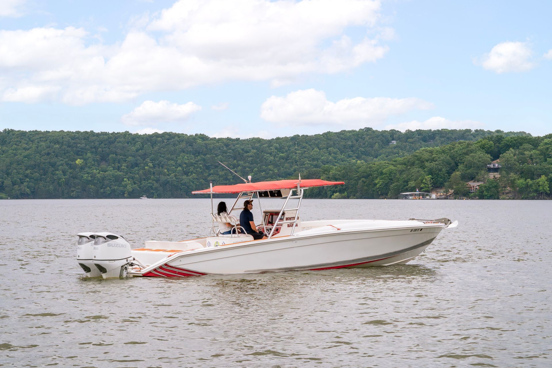 Motorboat with red canopy on a lake, two people aboard, wooded shoreline in the background