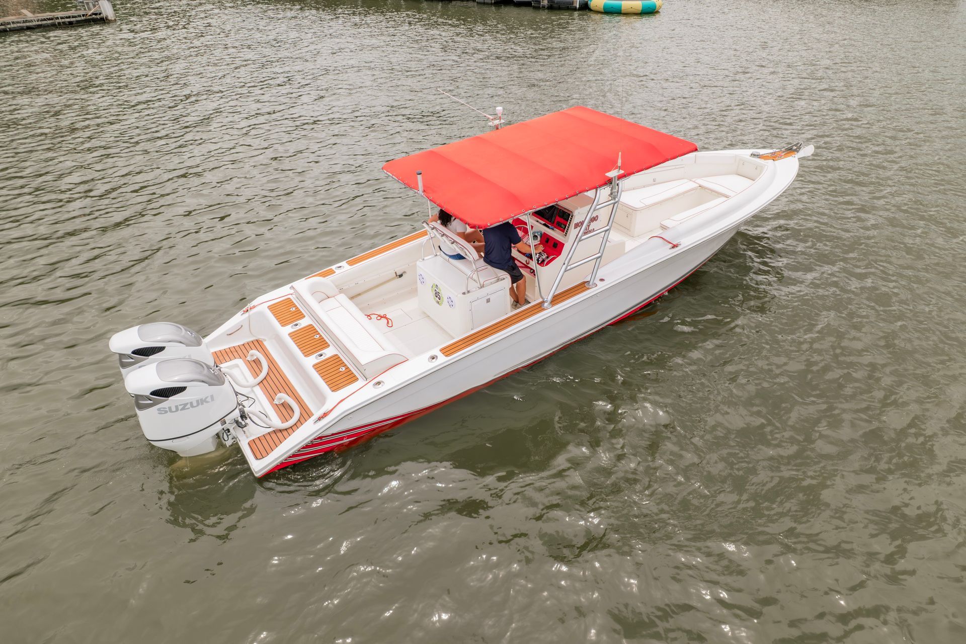 White motorboat with a red canopy floating on calm water, viewed from above