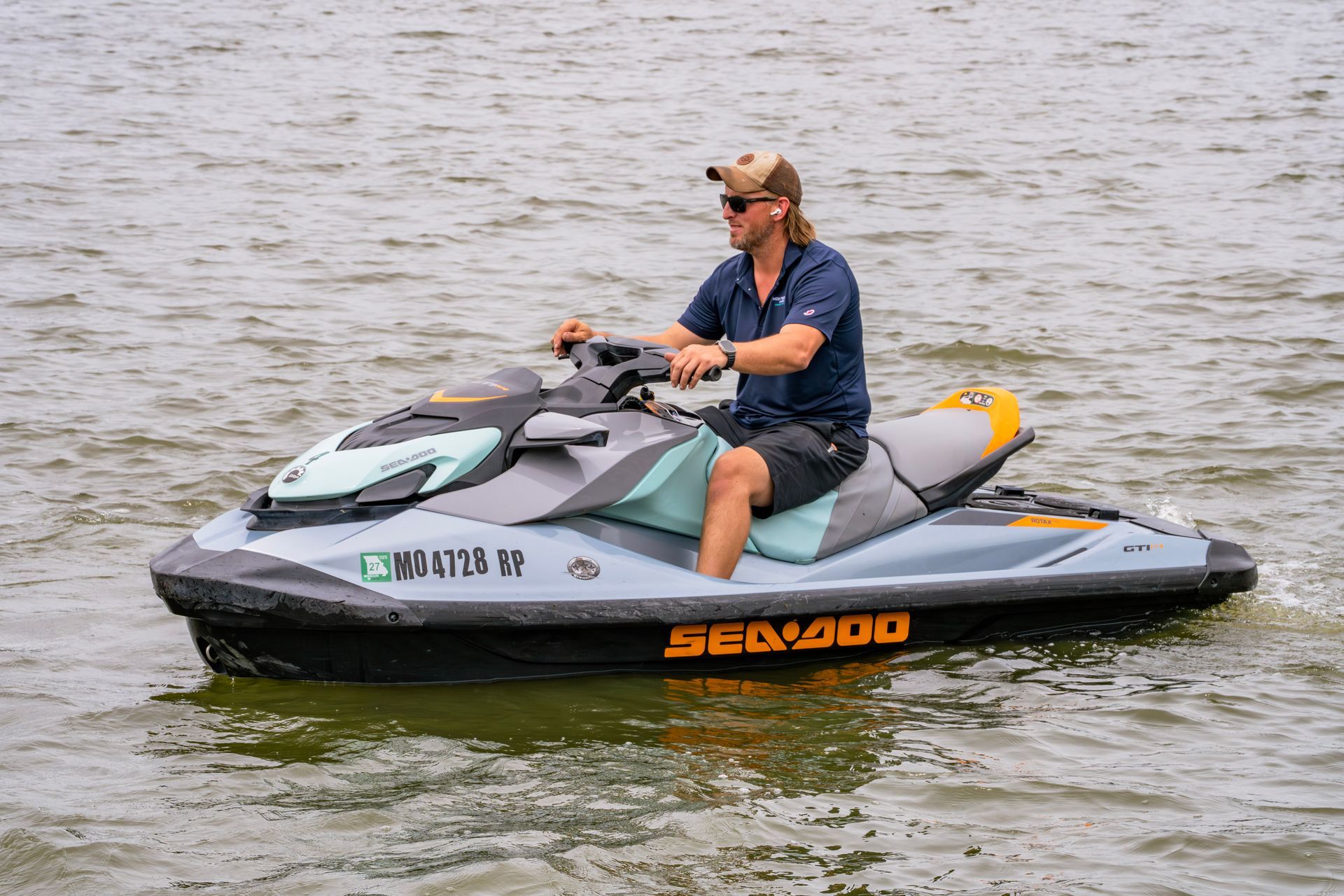 Person riding a gray and orange Sea-Doo jet ski on calm water