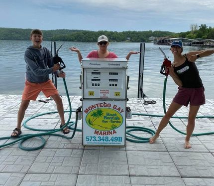 Three people posing with fishing rods beside a catch station on a dock by the water.