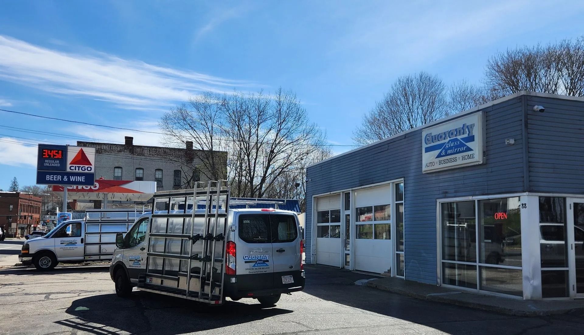 A delivery van with glass racks parked outside a blue glass shop under a partly cloudy sky.