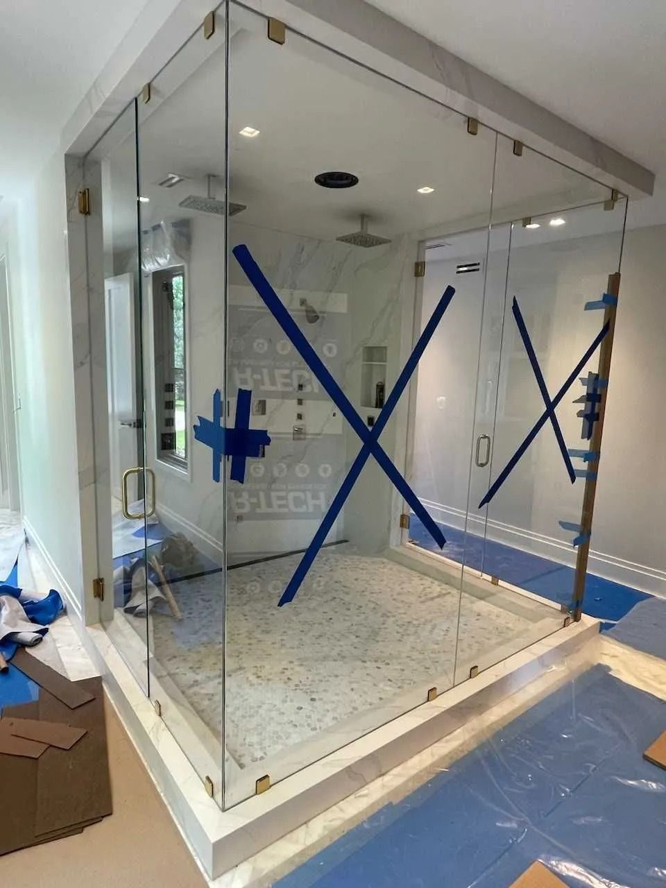 Glass shower enclosure, brass hardware, marble accents, blue tape, interior construction.