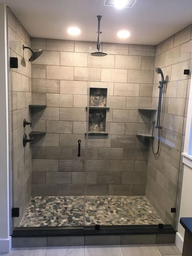 Modern shower with stone-like tile walls, glass door, pebble floor, built-in shelves, and multiple showerheads.