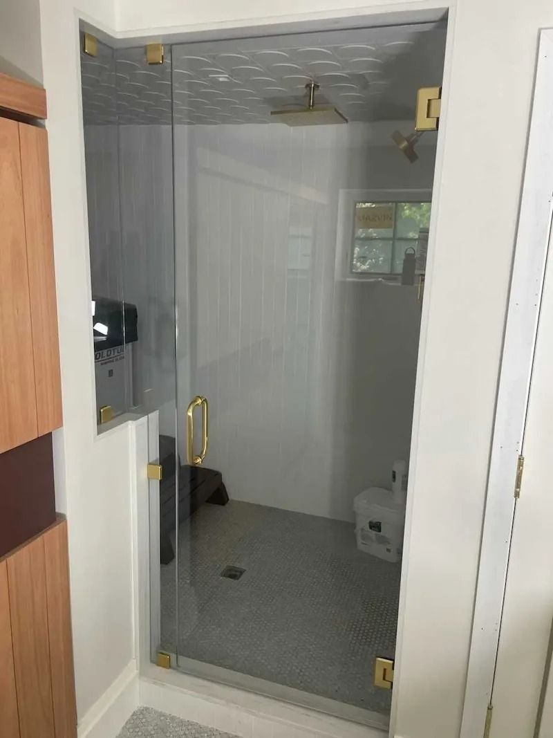 Glass shower enclosure with gold hardware in a bathroom.