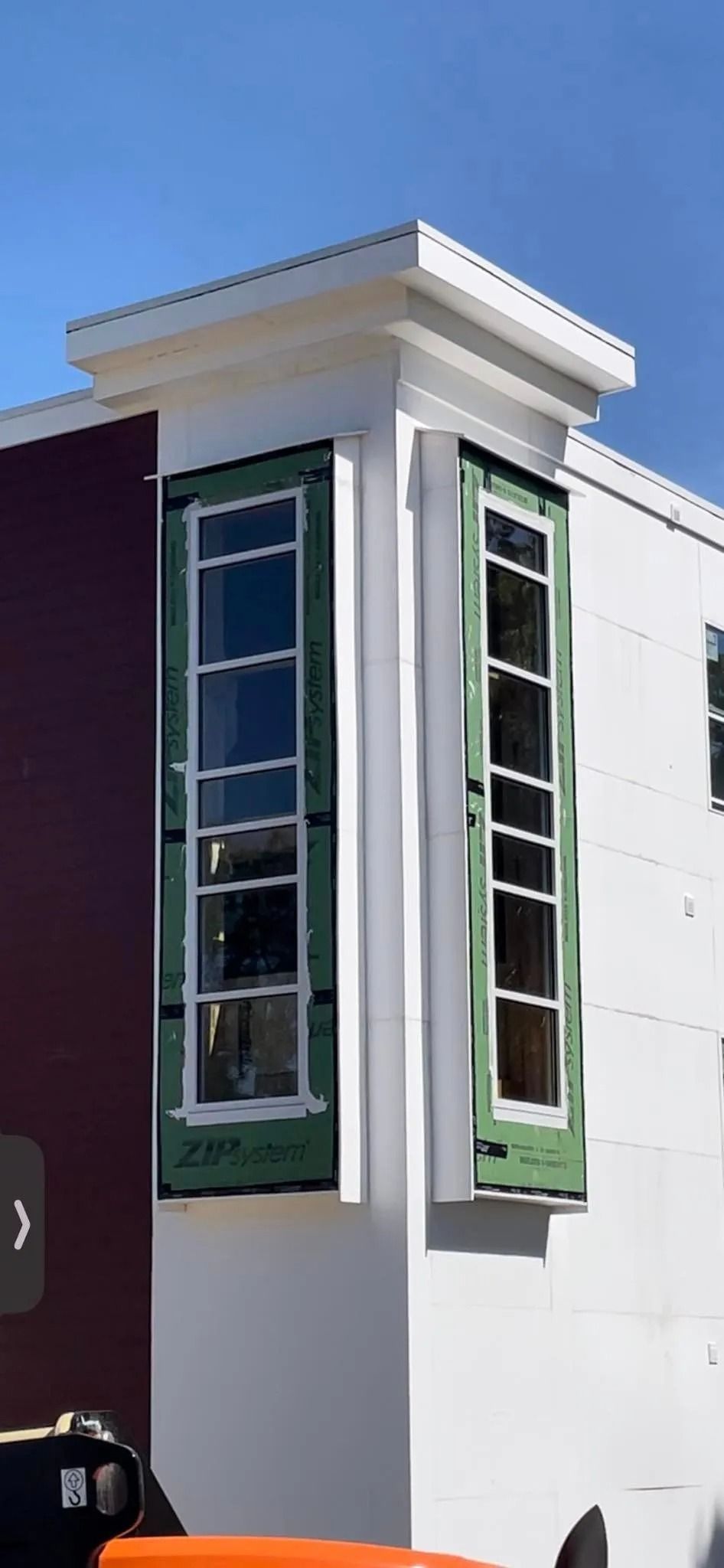 Corner of building with two tall windows under construction, white walls, dark green trim, and blue sky.