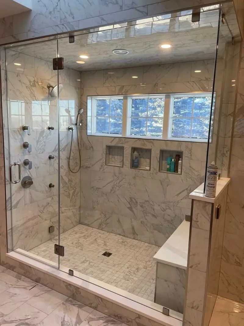 Spacious marble shower with glass doors, multiple showerheads, and a built-in bench.