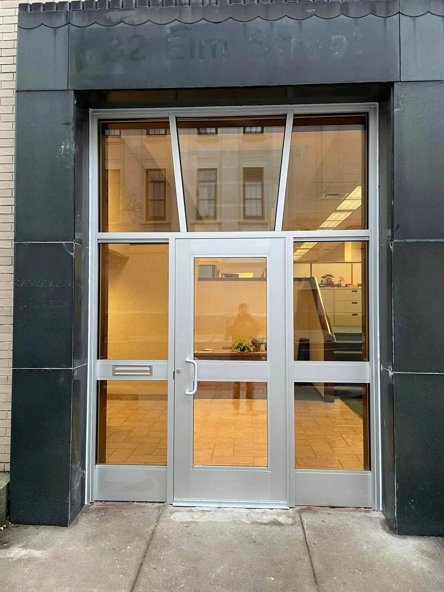 Silver framed door with glass panels reflecting a light interior. Black trim frames the entry.