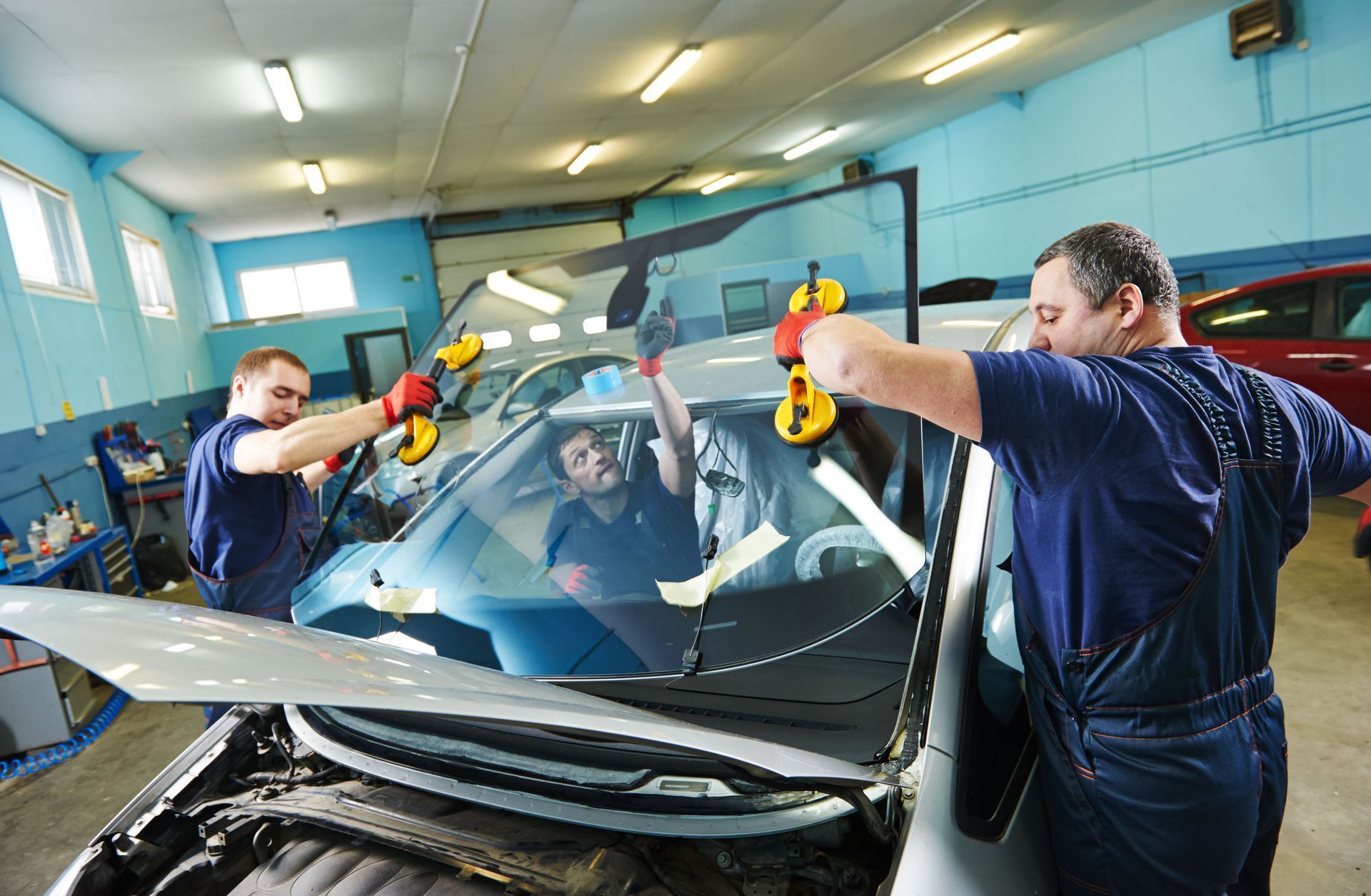 Three auto mechanics installing a windshield in a garage.