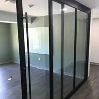 Black-framed glass partition with a door, dividing two rooms. Includes a white board.