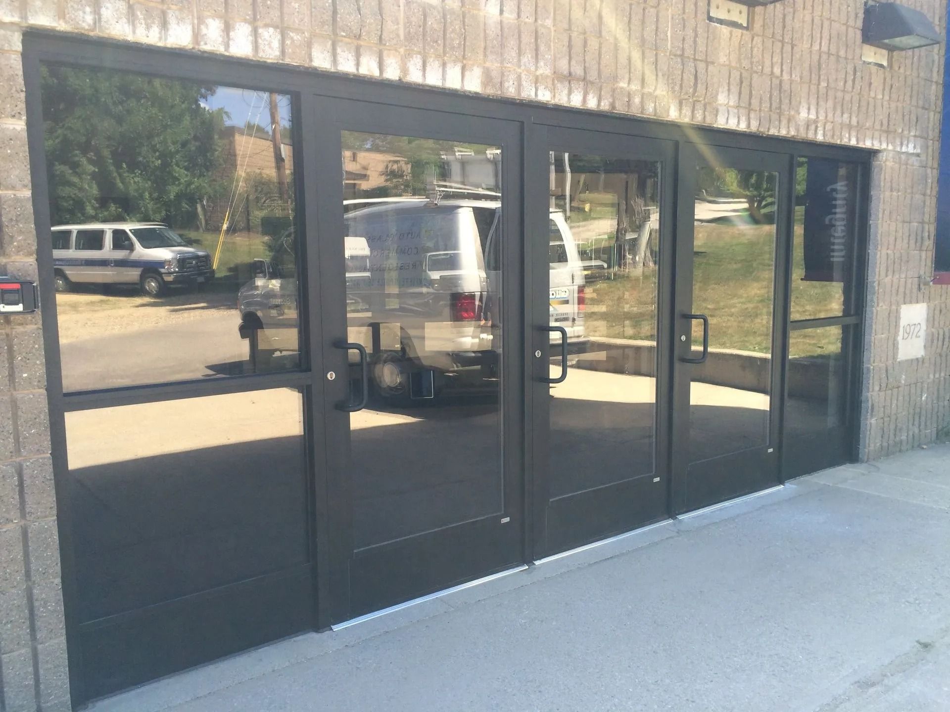 Exterior view of commercial building with tinted glass doors reflecting street scene; gray frames, brick exterior.