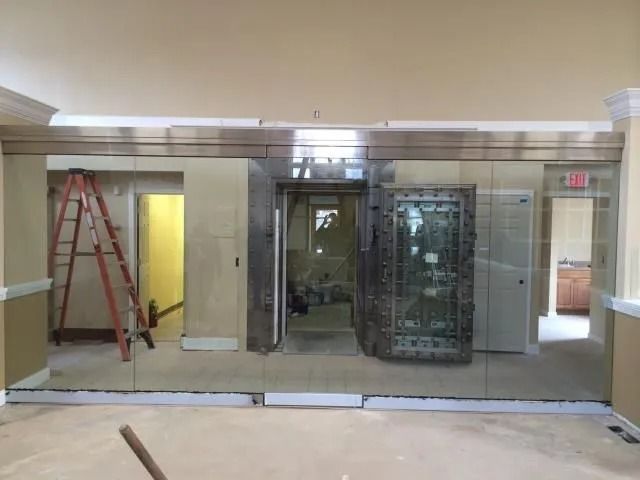 Interior room with a large, ornate safe door; mirrored wall; unfinished construction.