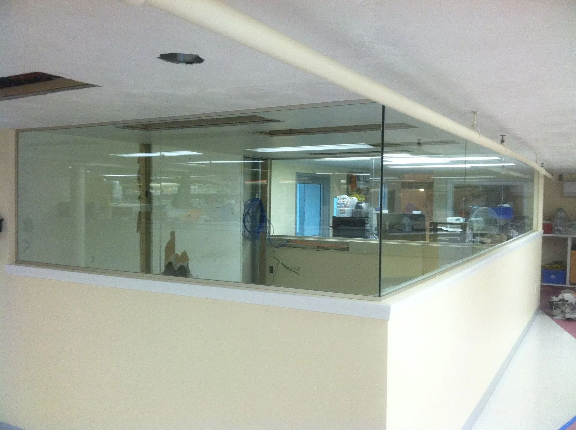 A room with a glass partition and beige walls. Visible office space is behind the glass.