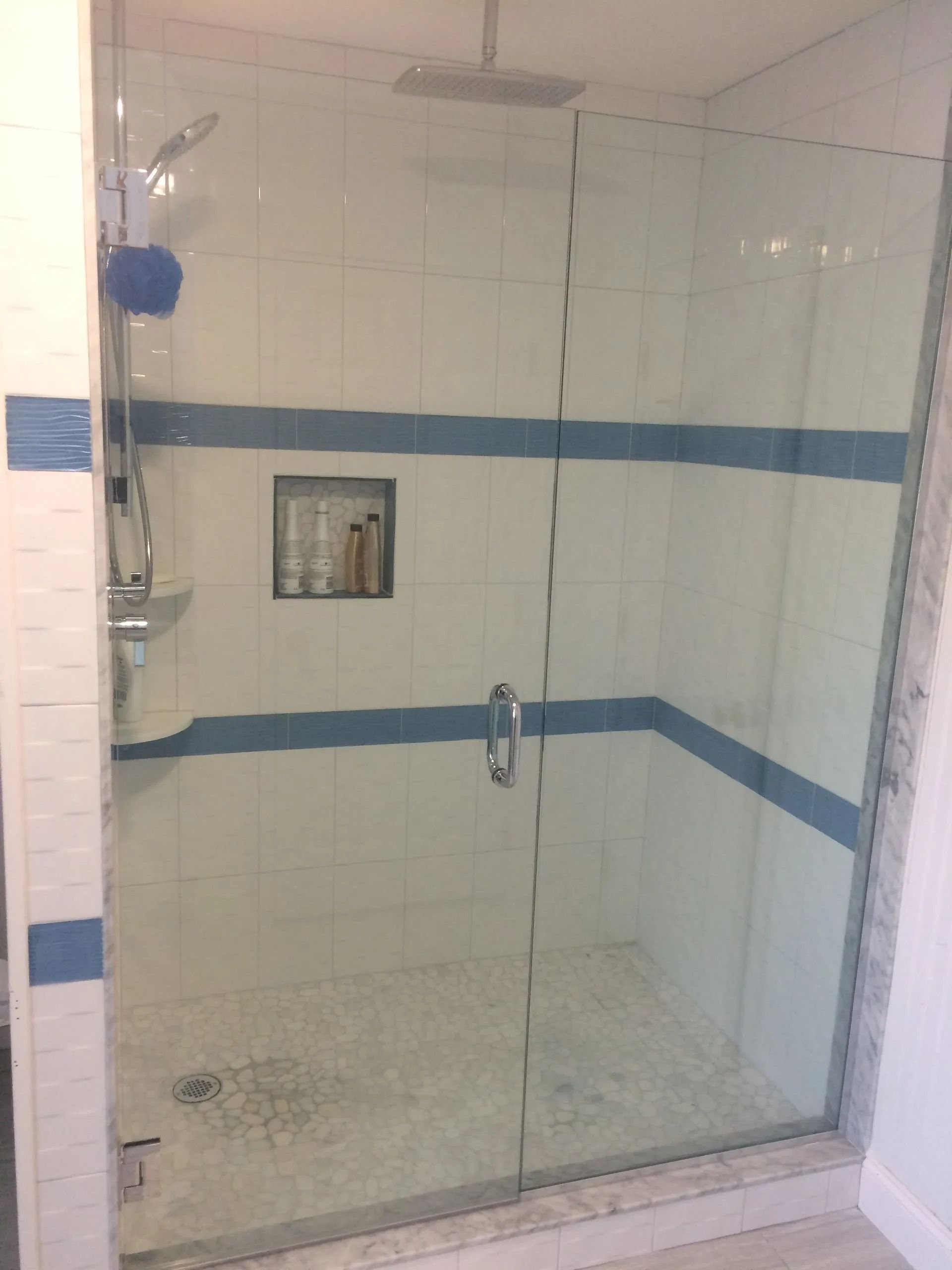 Glass shower with blue accent tiles, white walls, and a recessed shelf.