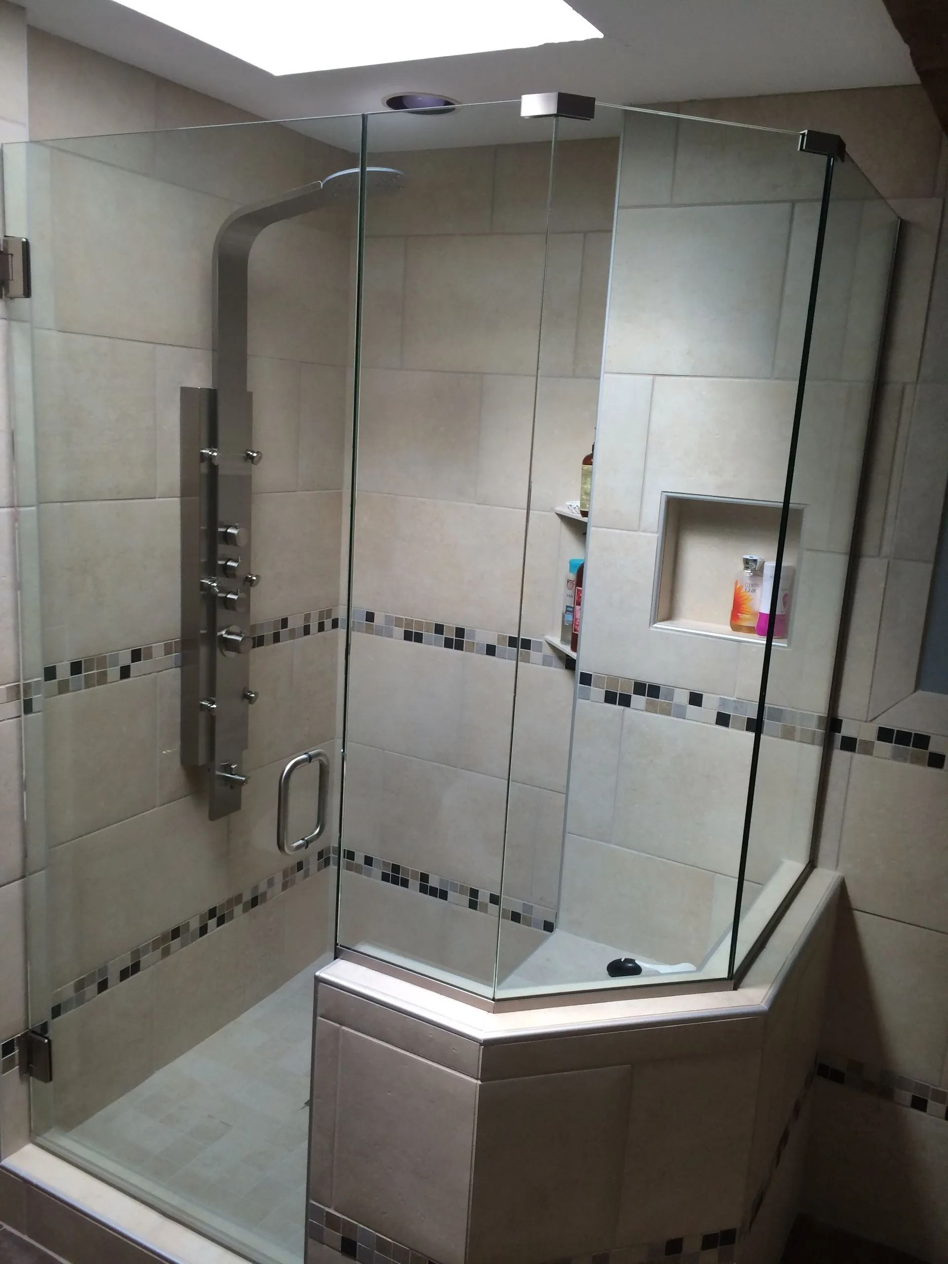Glass shower enclosure with tiled walls and a recessed shelf.