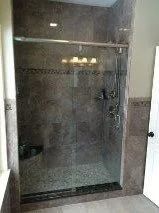 Glass-enclosed shower with gray tiled walls and floor, and chrome shower fixtures.